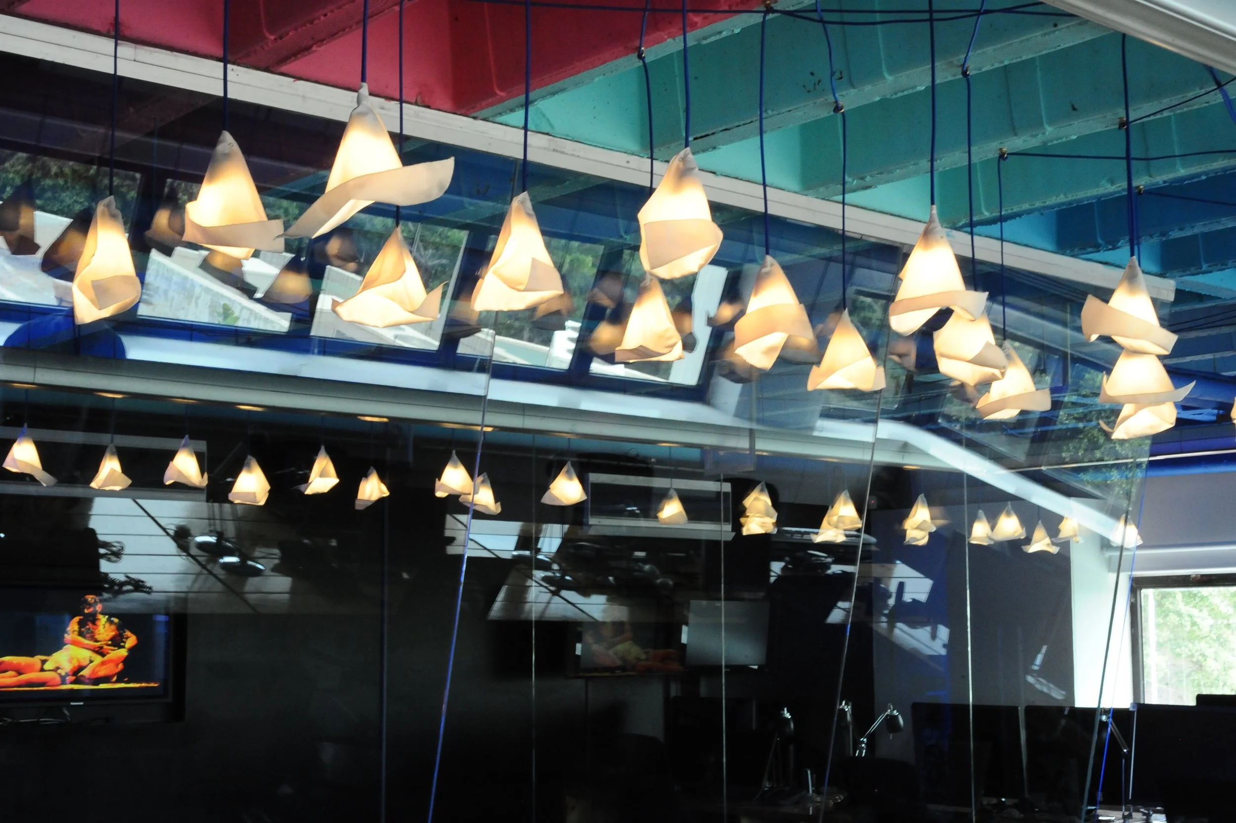 A row of modern hanging pendant lights in a contemporary interior space with glass walls, reflecting the lights and the outdoor scenery.