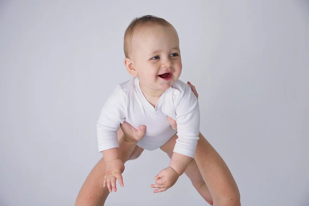 Baby playing aeroplanes in mums arms smiling in 10 month old photoshoot.