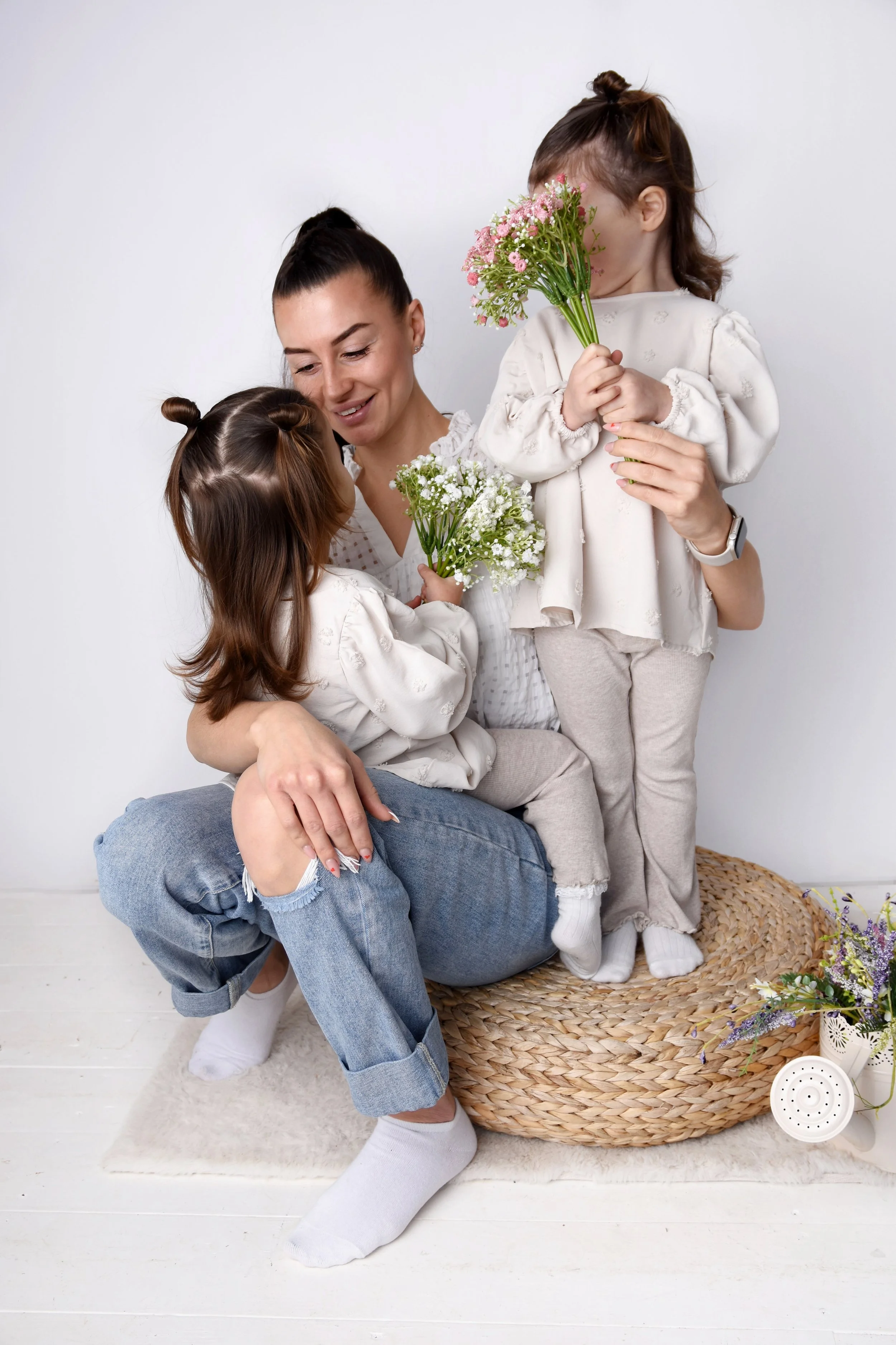 Mother cuddling her daughters. They are holding flowers for her and she is smiling down at one of them.