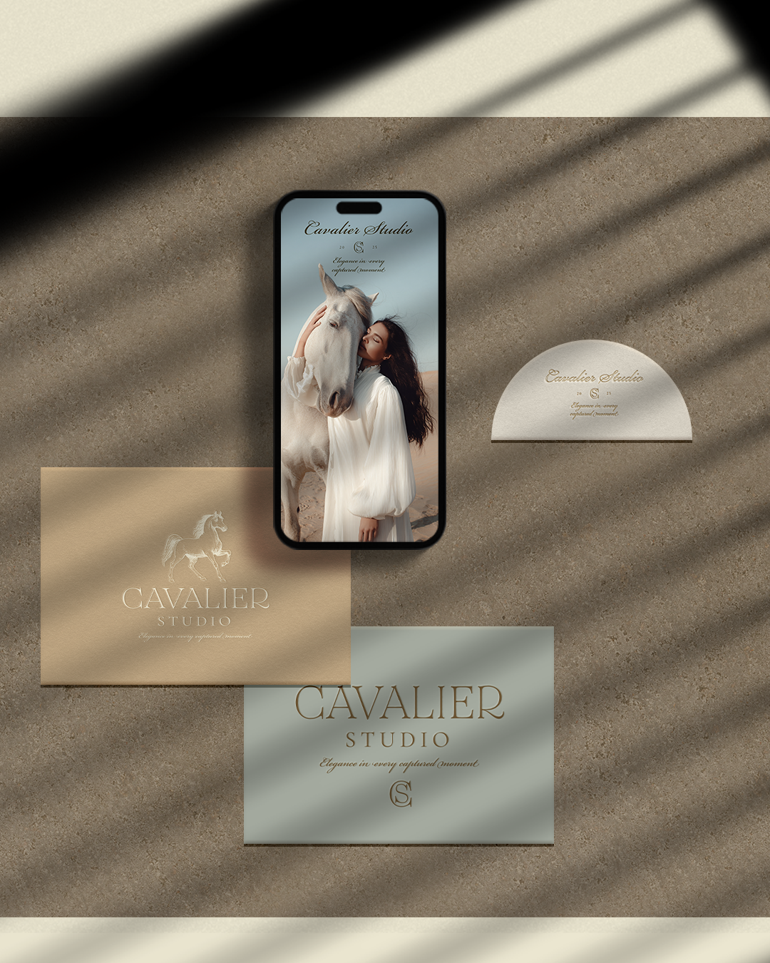 A flat lay smartphone and stationery items on a sandy surface featuring Cavalier Studio branding, including a photo of a woman and a horse, and various cards.
