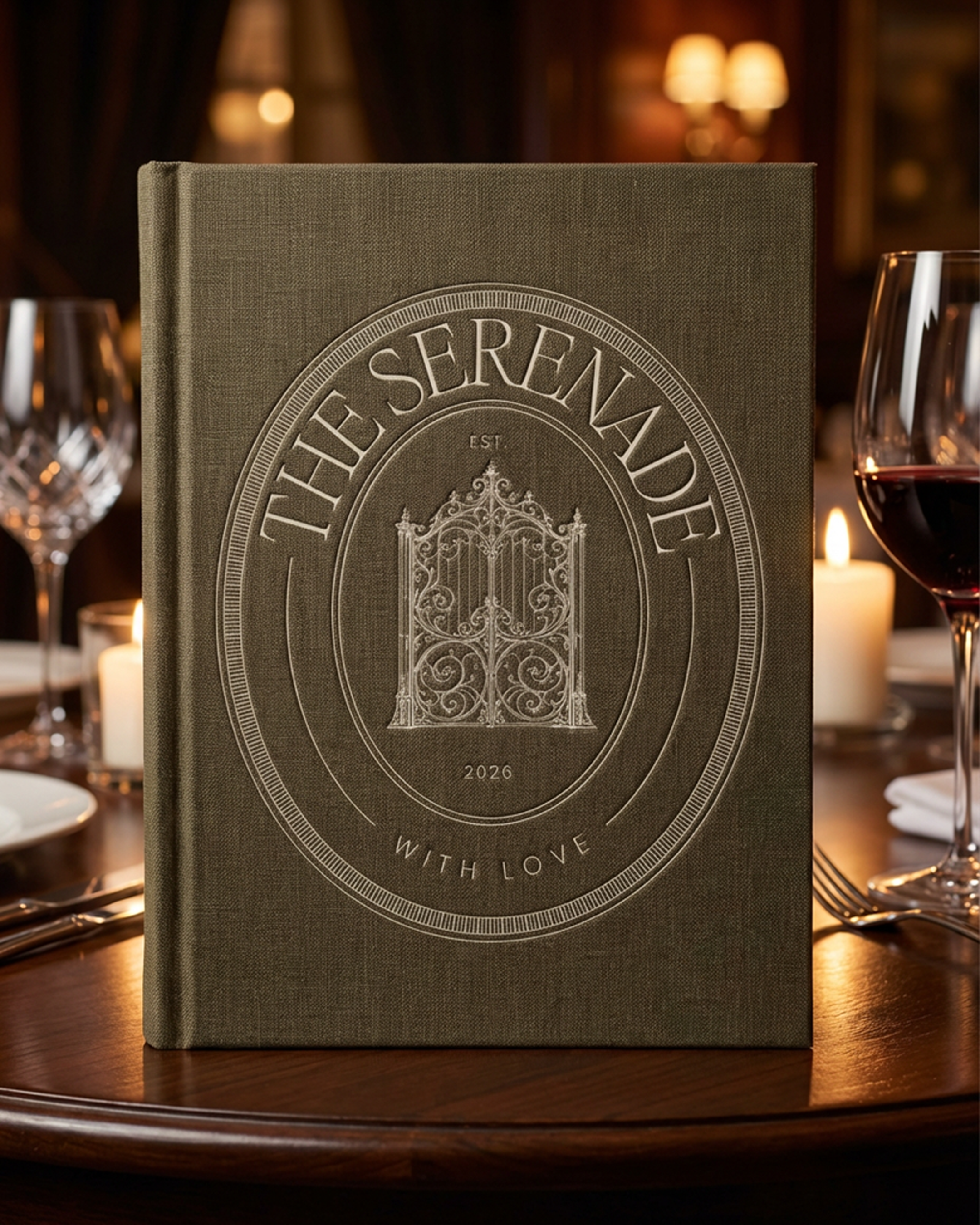 A hardcover book titled 'The Serene' is placed on a dining table set with wine glasses, candles, and silverware. The background features a warm, dimly lit room.