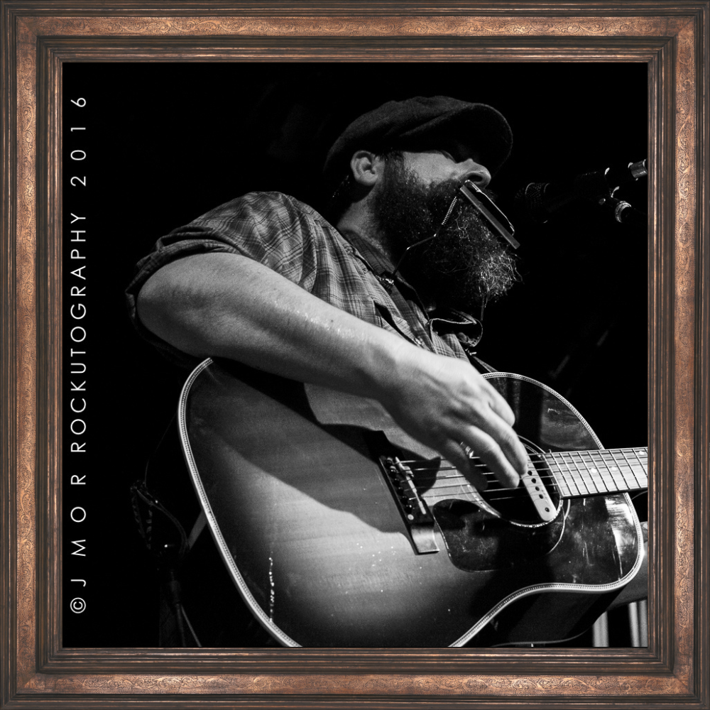 Black-and-white photograph of Chad Bault performing onstage with an acoustic guitar.