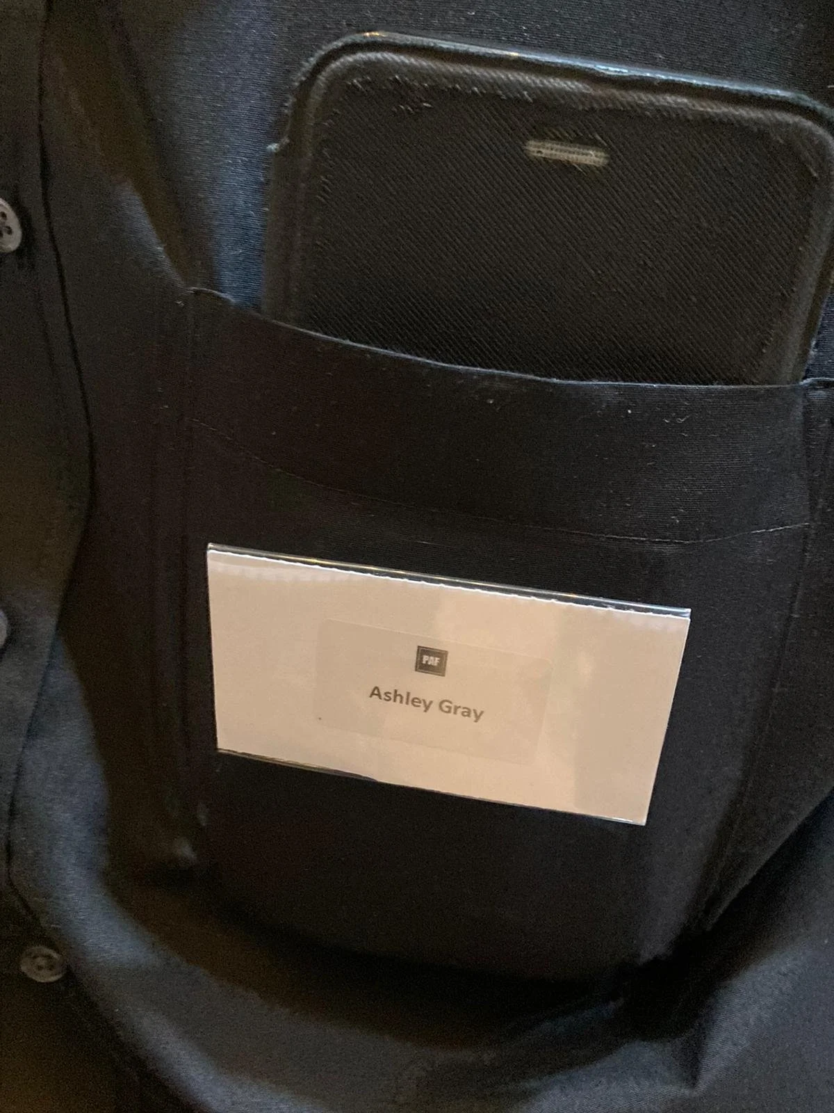 Back pocket of a black bag with a name tag that reads 'Ashley Gray'.