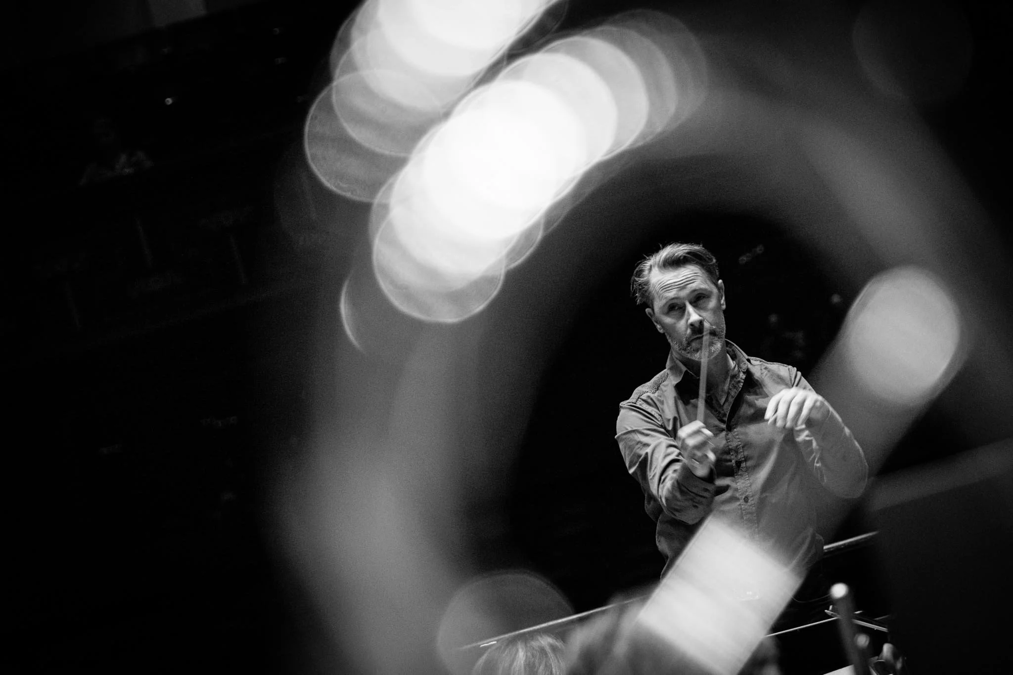A man conducting, photographed through an instrument in an instrument from an orchestra - out-of-focus lights creating a bokeh effect.