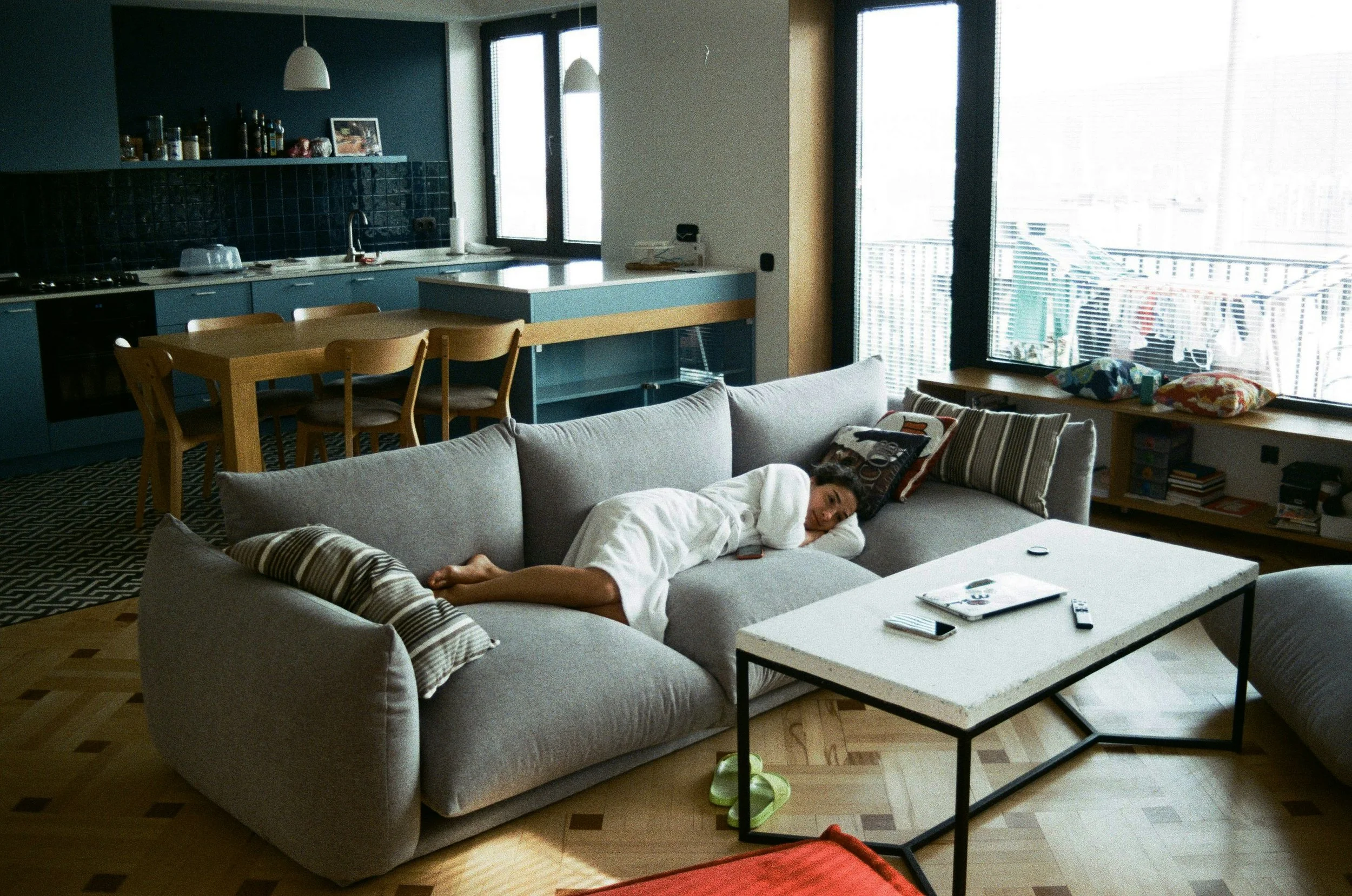 Woman lying still on a couch mid-afternoon, staring at the ceiling instead of her laptop, breaking old patterns of constant productivity.