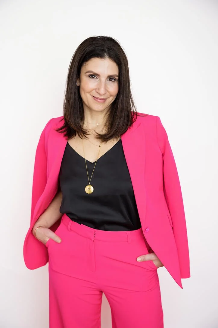 Michelle Pollack, Keynote Speaker on Leadership, wears a hot pink suit with a black camisole and stands with her hands in her pockets and a smile on her face.