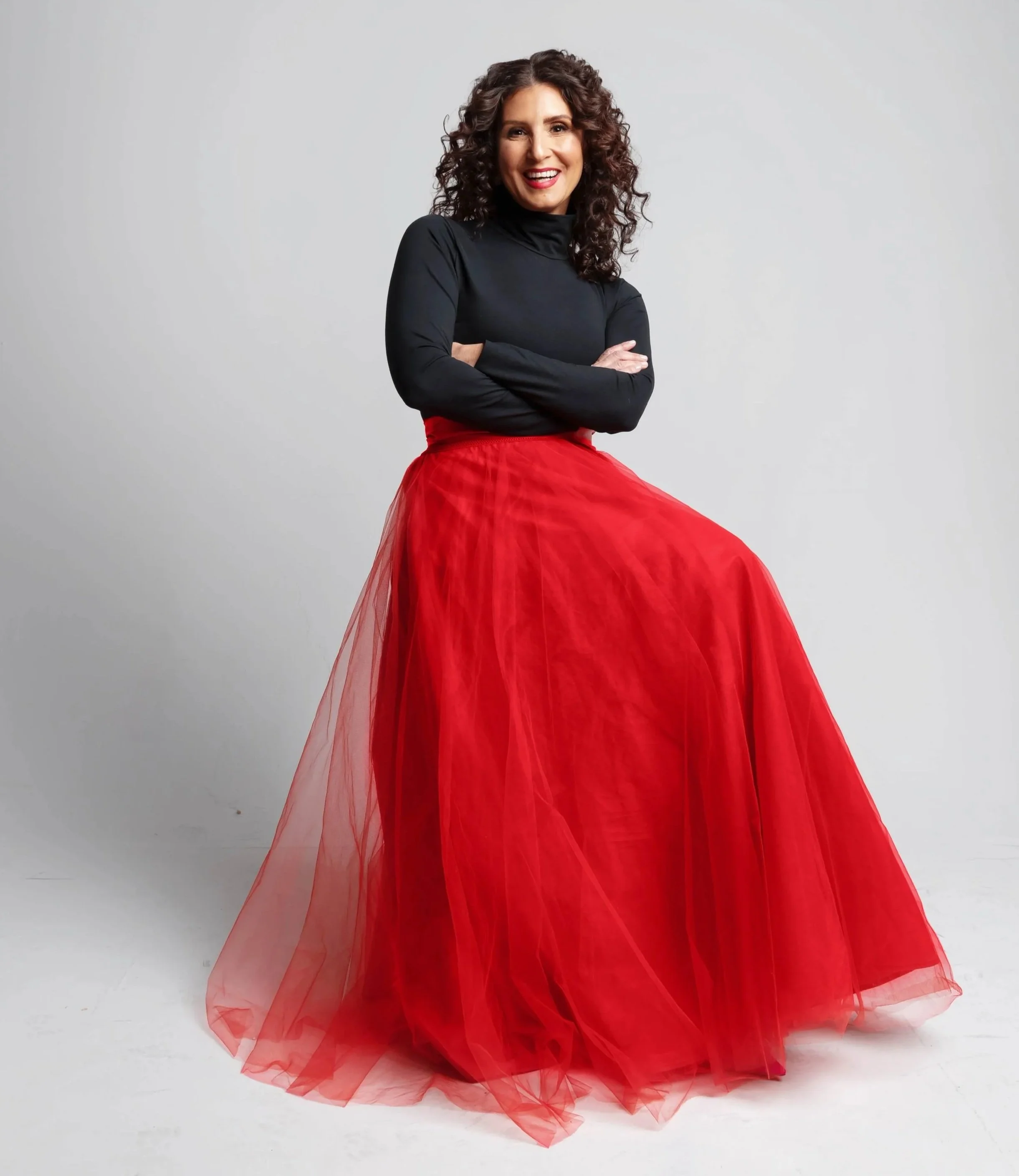 Michelle Pollack, self-leadership coach, sits on a stool with her arms crossed and a big smile on her face.