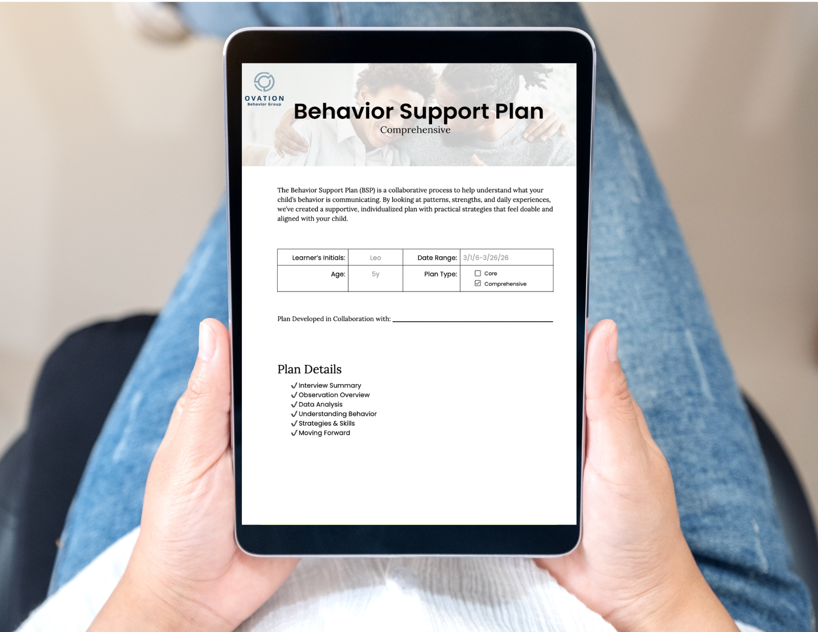 A young girl with short dark hair in a white long sleeve shirt sitting at a table, looking at a smartphone on the table, with a cartoon character on the screen.