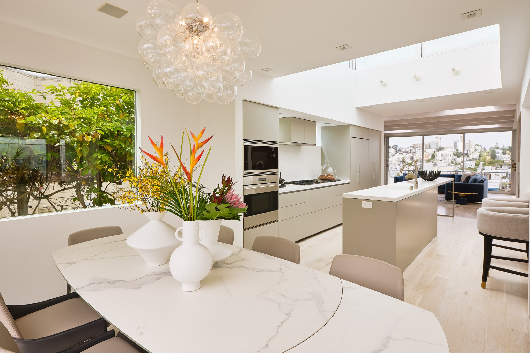 Modern open-concept kitchen and dining area in a bright apartment with a view of a cityscape.
