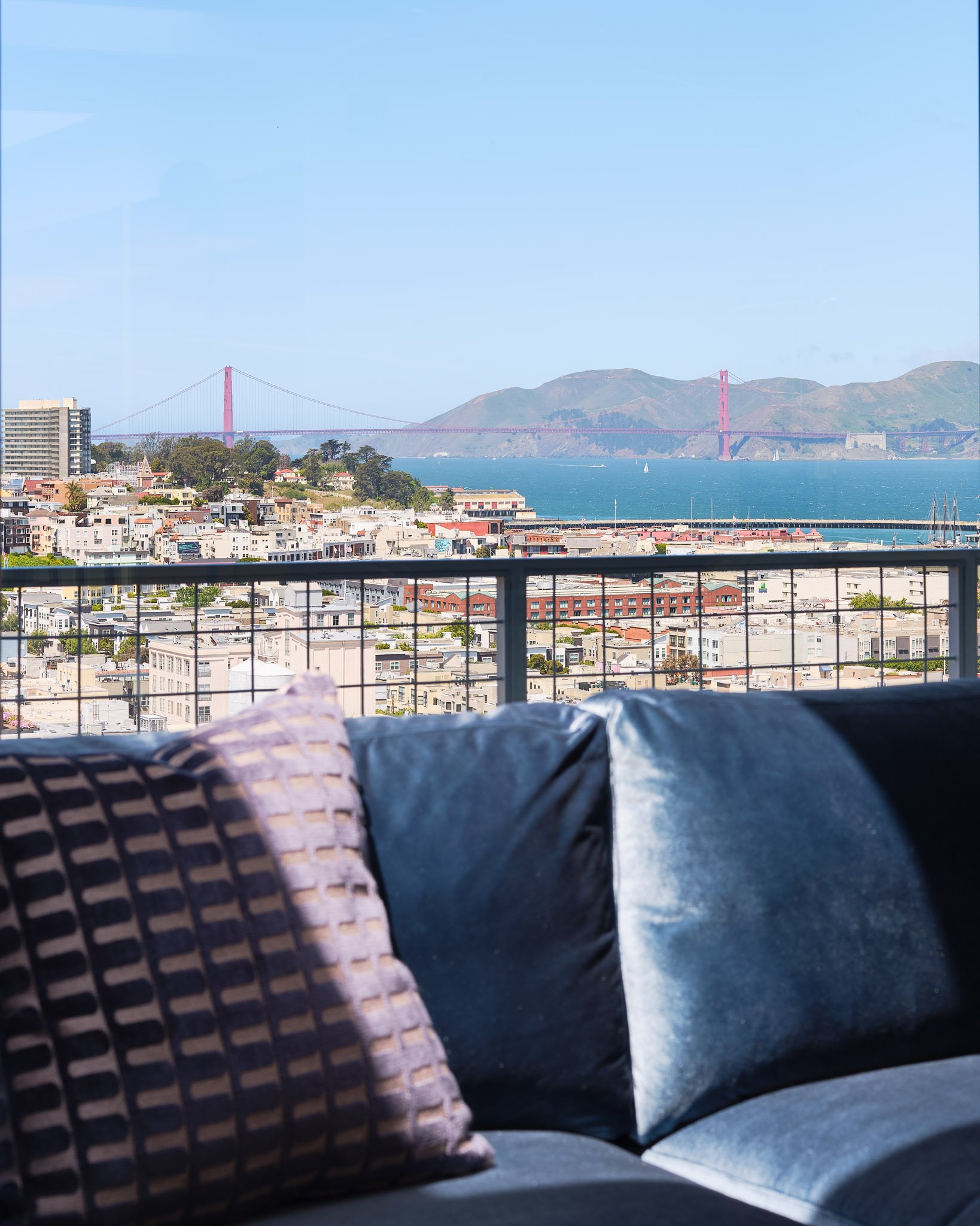 View of San Francisco skyline and Golden Gate Bridge from a balcony with pillows on a sofa.