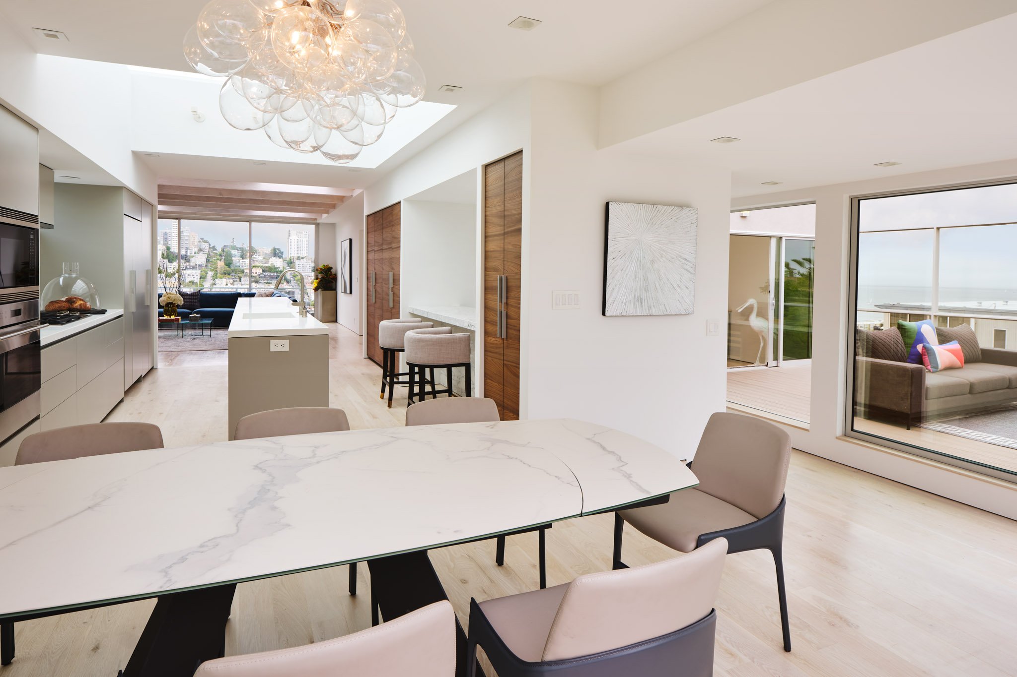 Modern open-concept living space with a dining table, kitchen area, outdoor balcony with seating, and city views