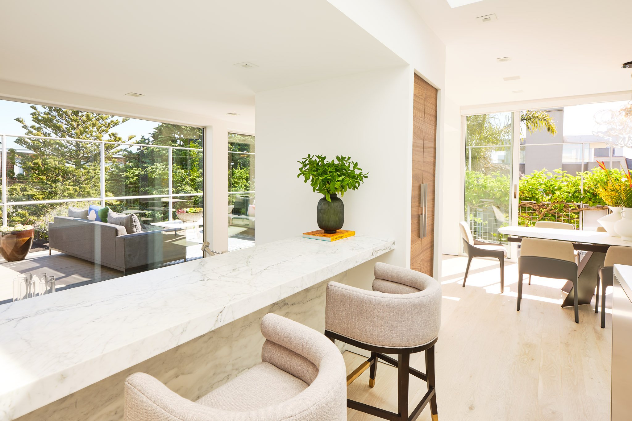 Bright modern kitchen and living room with large glass doors and trees outside.