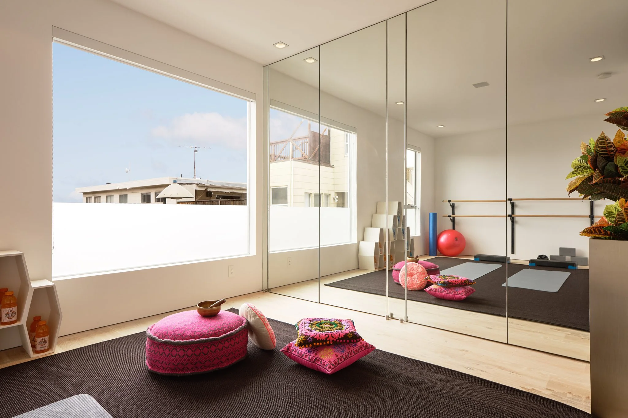 Exercise or yoga room with large windows, mirrors, pink cushions, exercise mats, a red exercise ball, a blue yoga mat, and a stretching bar.