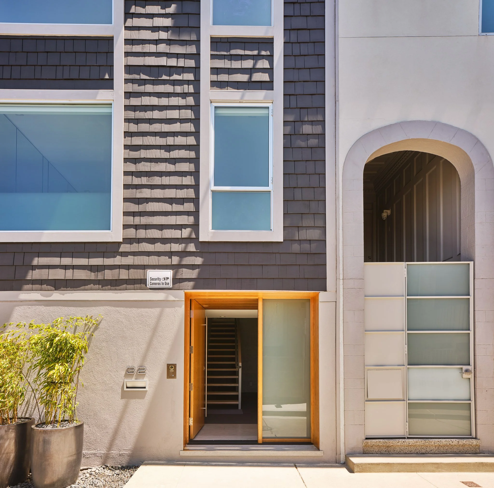 Modern apartment building entrance with a wooden door, potted plants, and large windows.