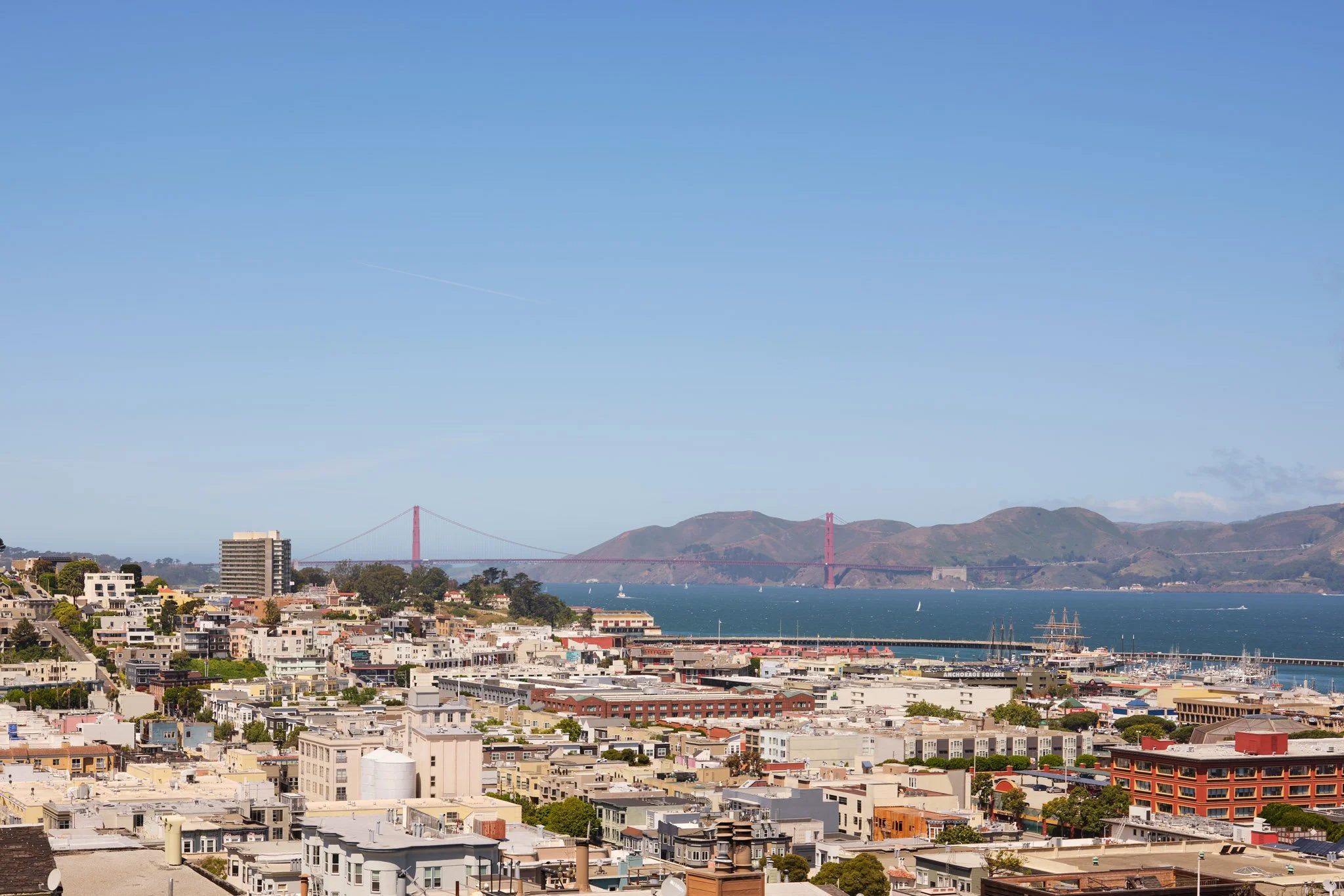 View of San Francisco skyline with the Golden Gate Bridge in the background on a clear day, including residential and commercial buildings in the foreground.