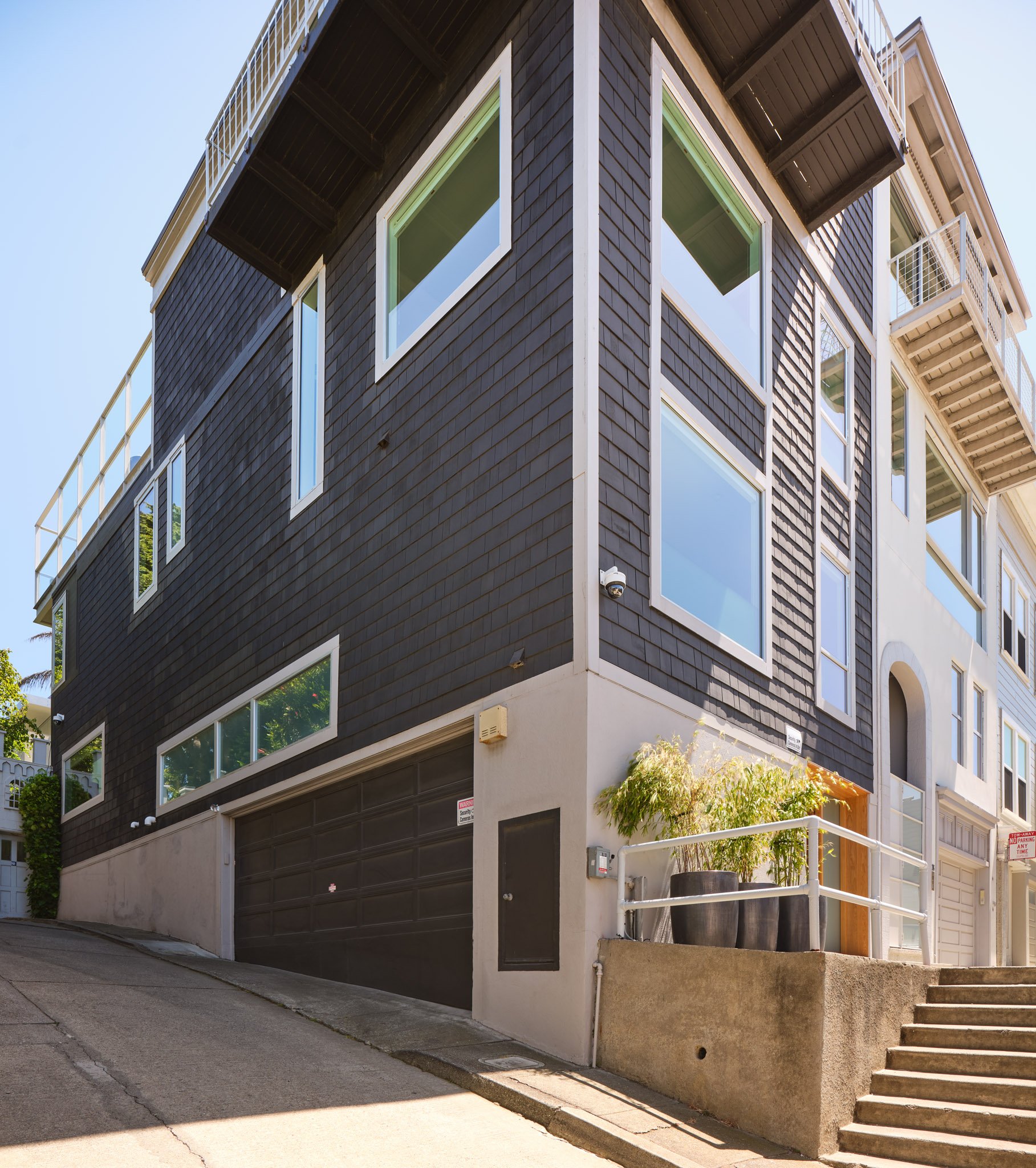 Modern multi-story building with black and white exterior, large windows, a garage, and outdoor staircase with planters.