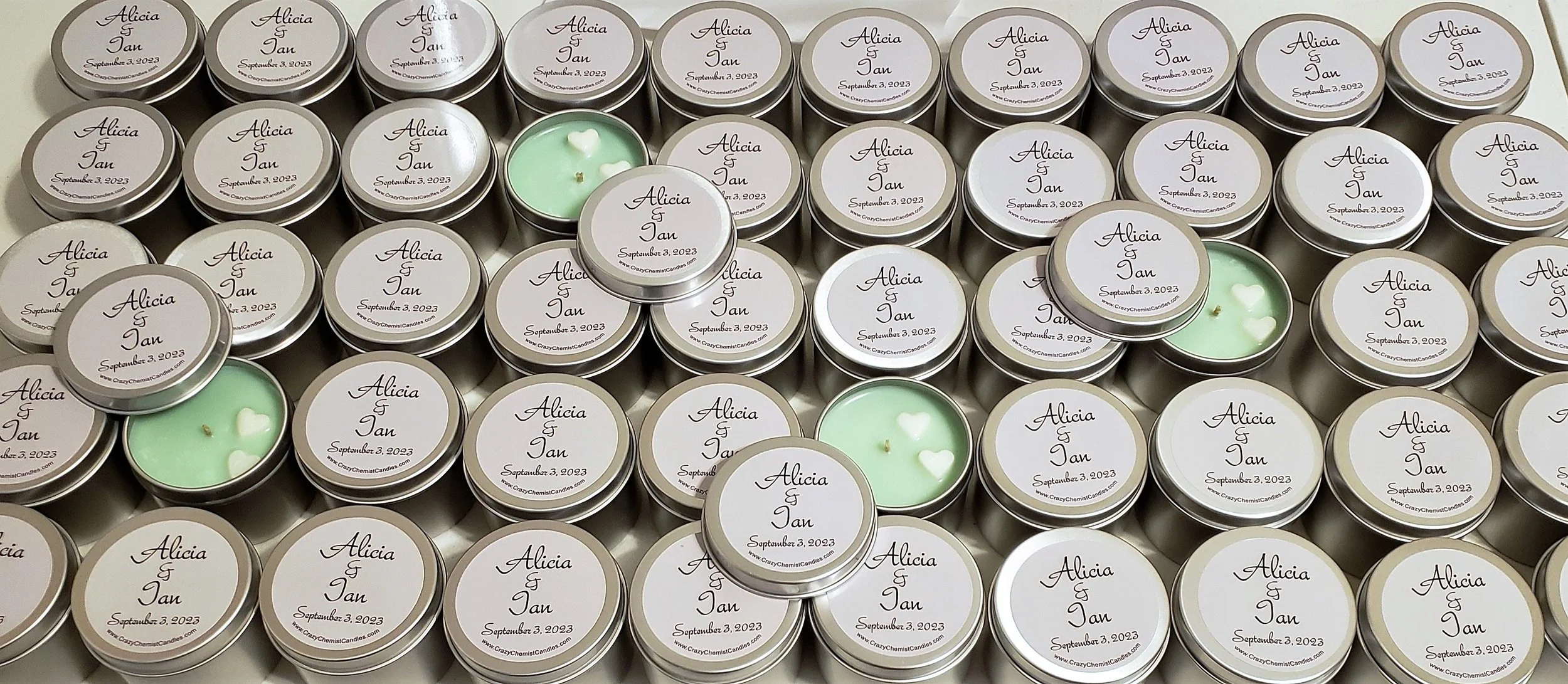 Multiple small metal tins with custom labels, some contain green candles with heart-shaped wax details.