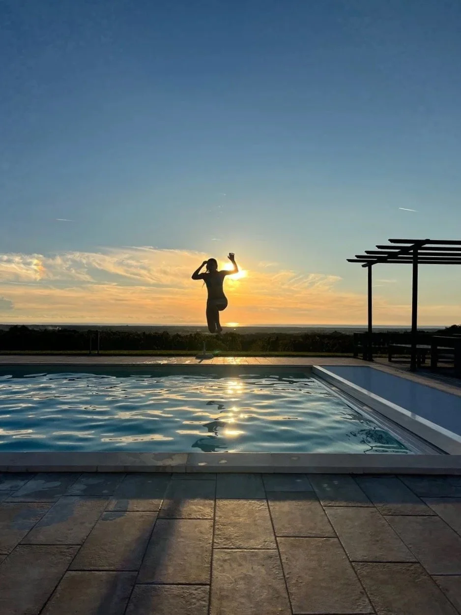 Elev som hopper ut i bassenget i soldnedgang med havet i bakgrunnen