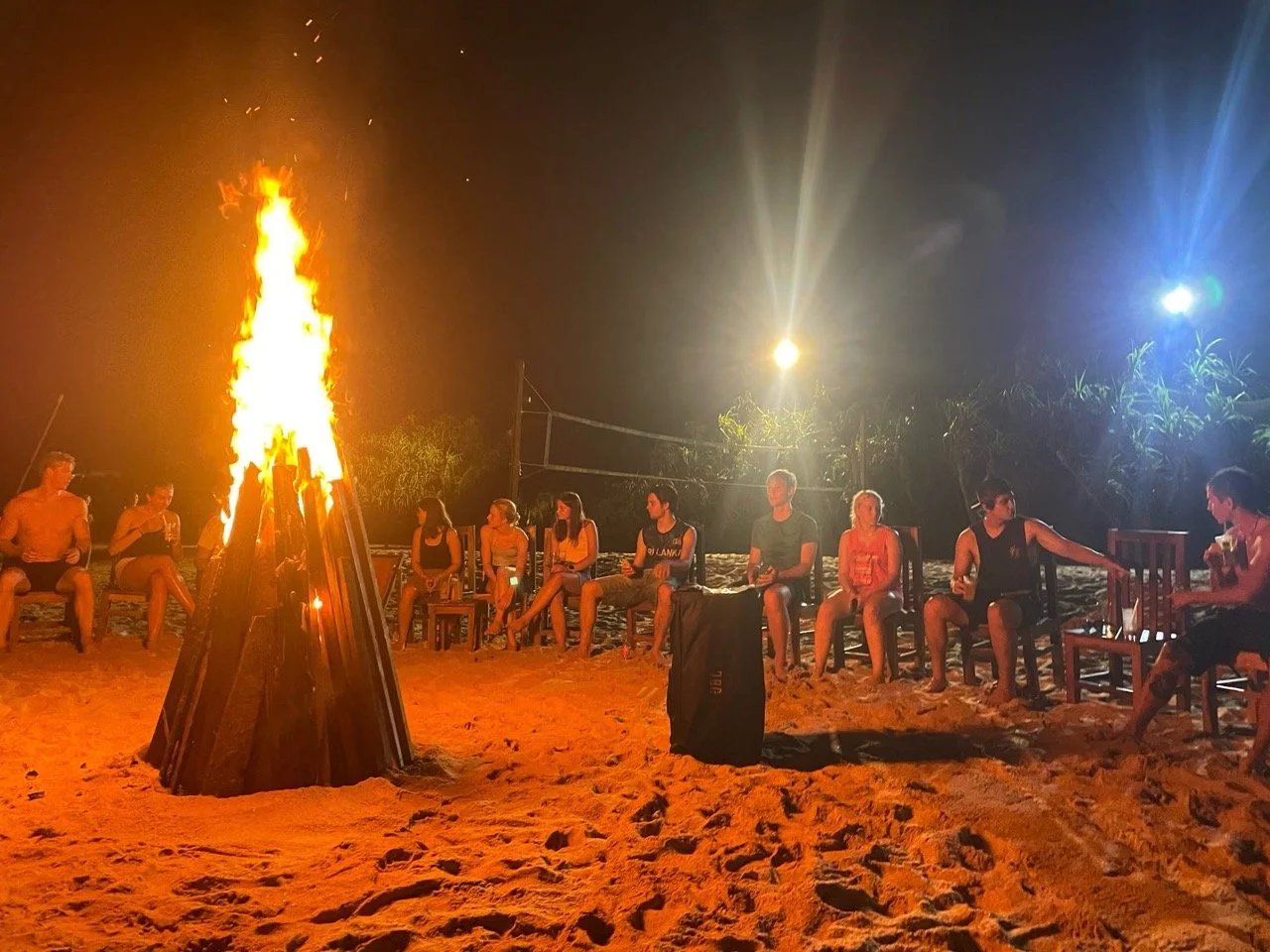 Elever koser seg rundt et bål på stranda rett ved sandvolleyball-banen på kvelden i Sri Lankai