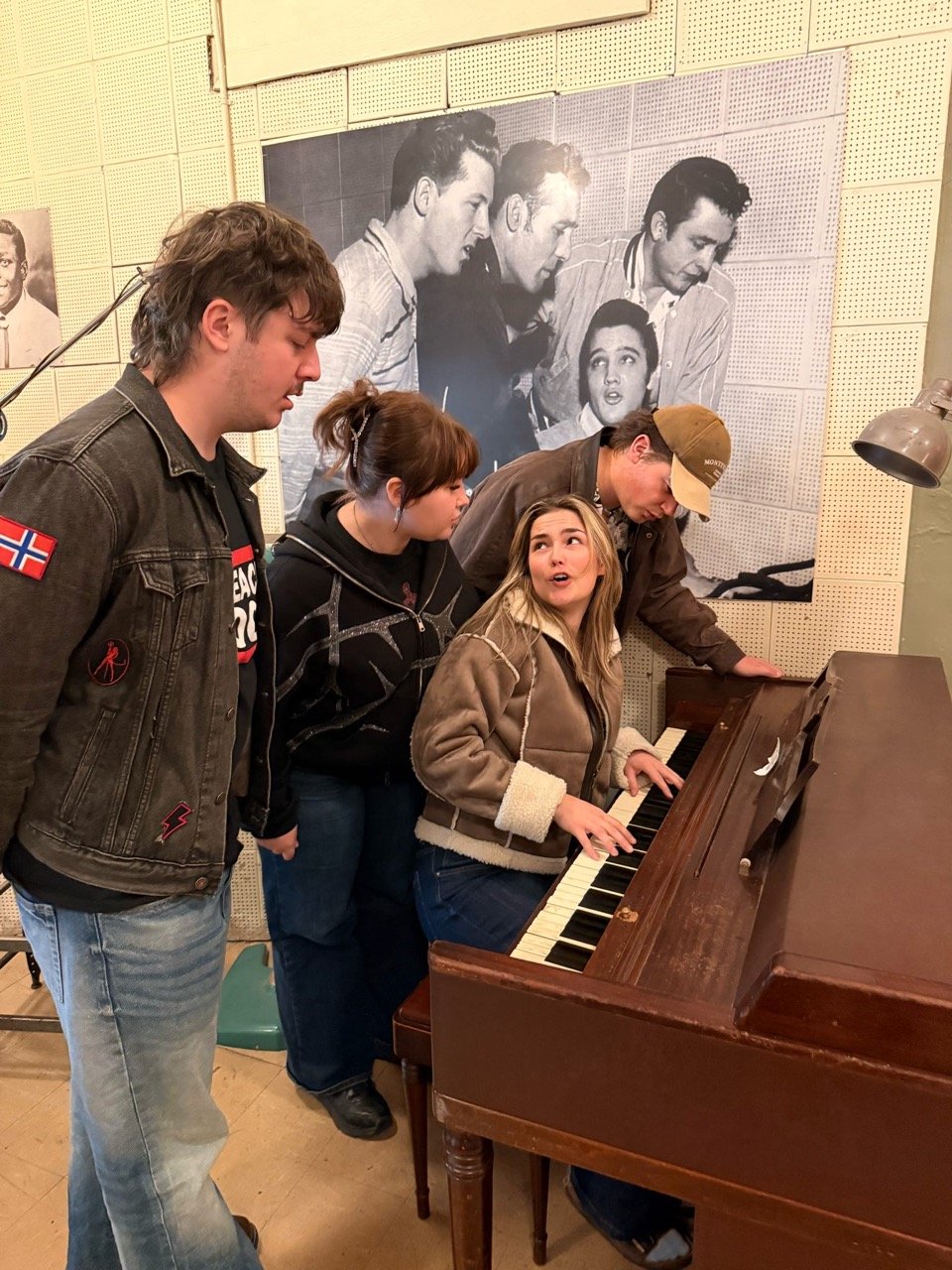 Musikk elever i Sun studio som spiller på Jerry Lee Lewis sitt piano og poser etter bilde av Elvis Presley, Jerry Lee Lewis med flere på bilde bak.