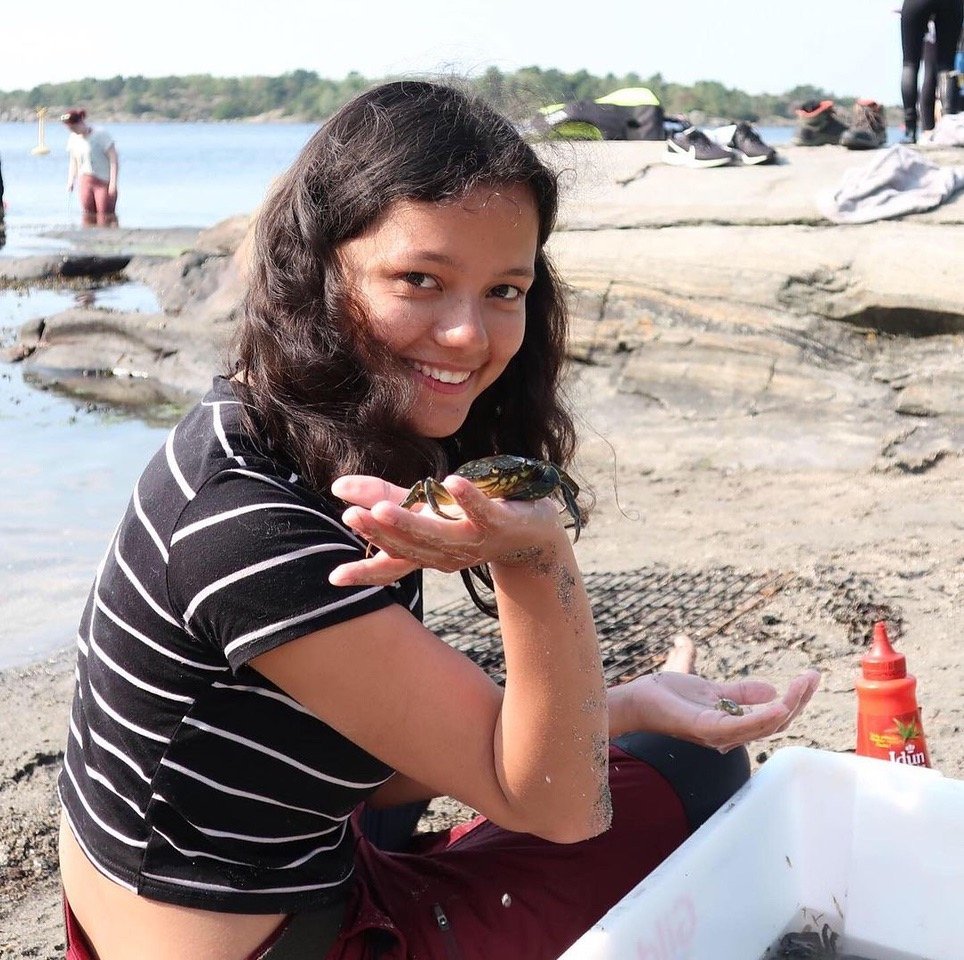 A student explores marine life by holding a crab during a hands-on learning activity along the Norwegian coast.