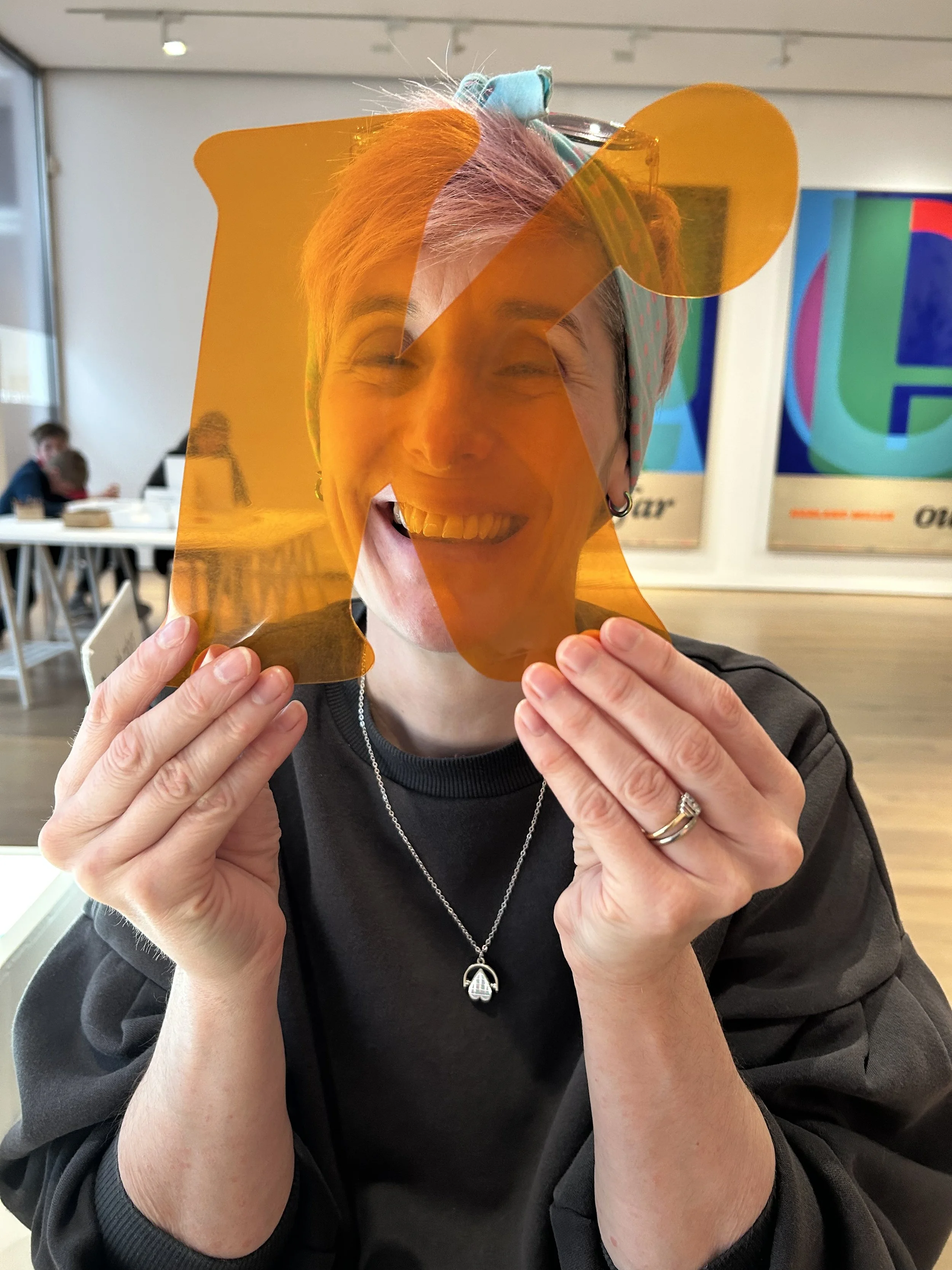 Artist Kim Bevan holds a large transparent letter K in front of her face