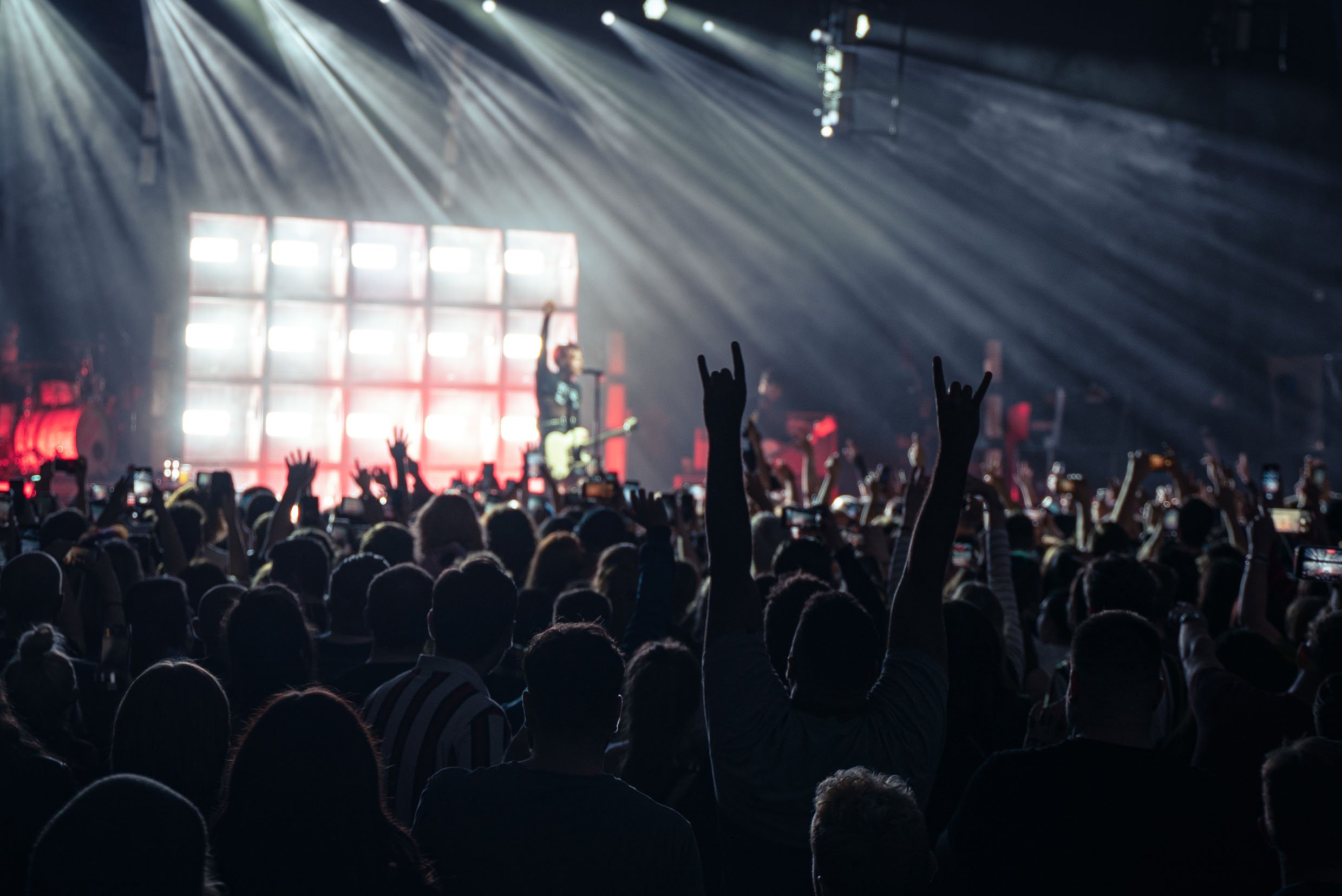 Crowd at a rock concert with raised hands and stage lighting.