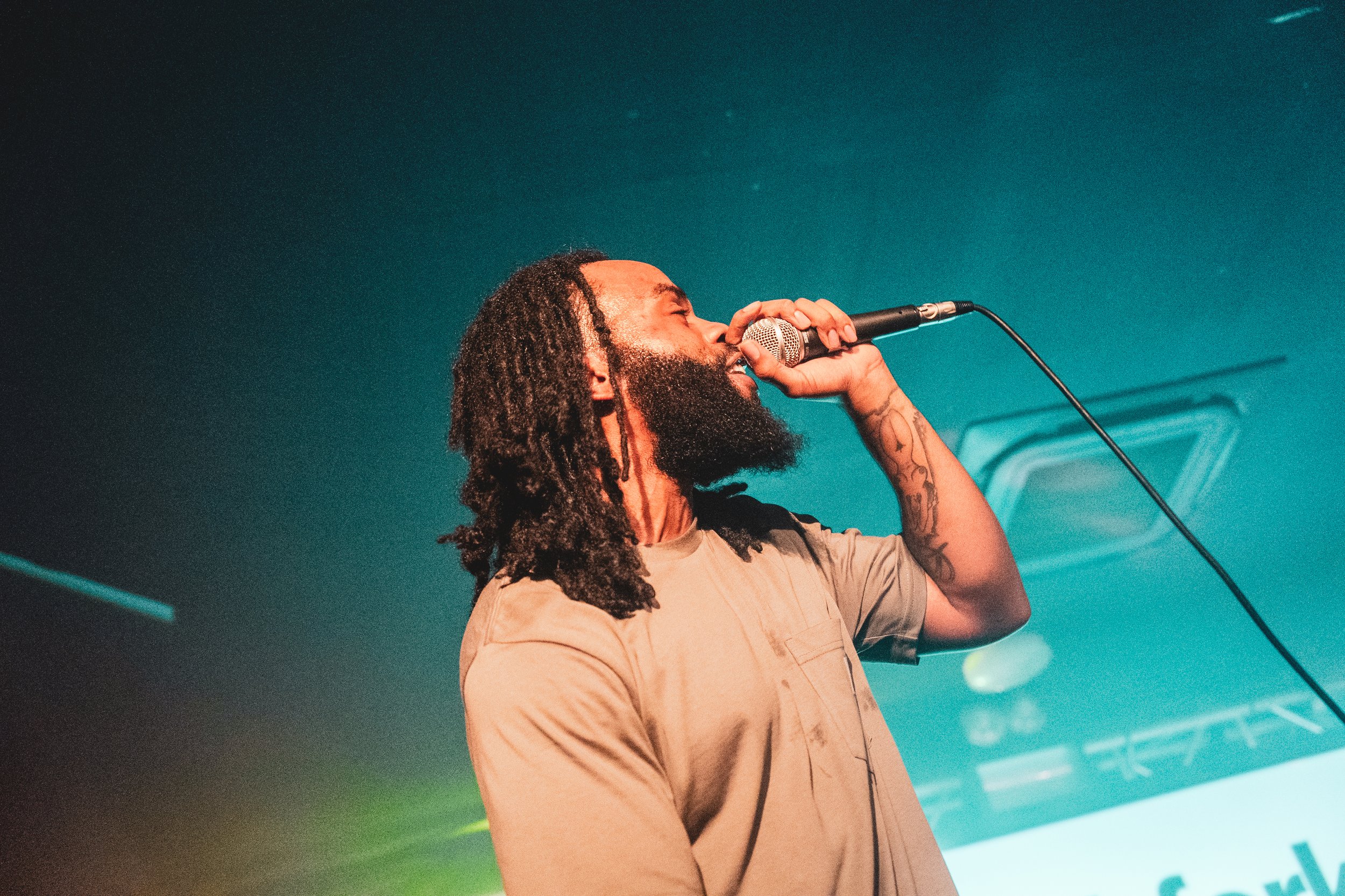 Man with dreadlocks singing into a microphone on stage.
