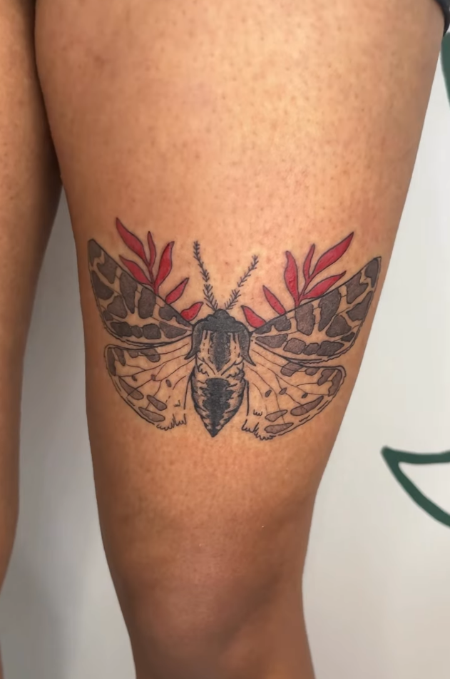 Tattoo of a moth with red leaves and plant details on a person's thigh.