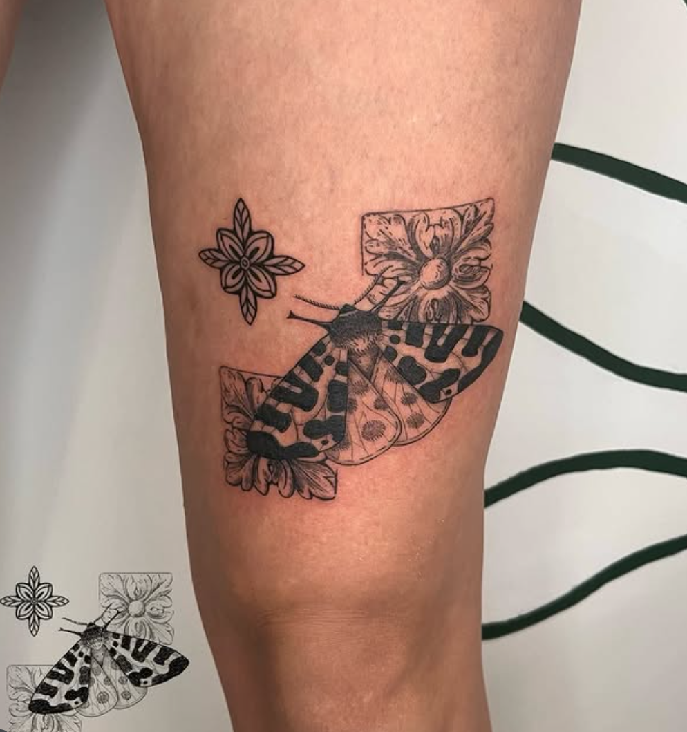 Tattoo of a butterfly with floral accents on a person's leg.