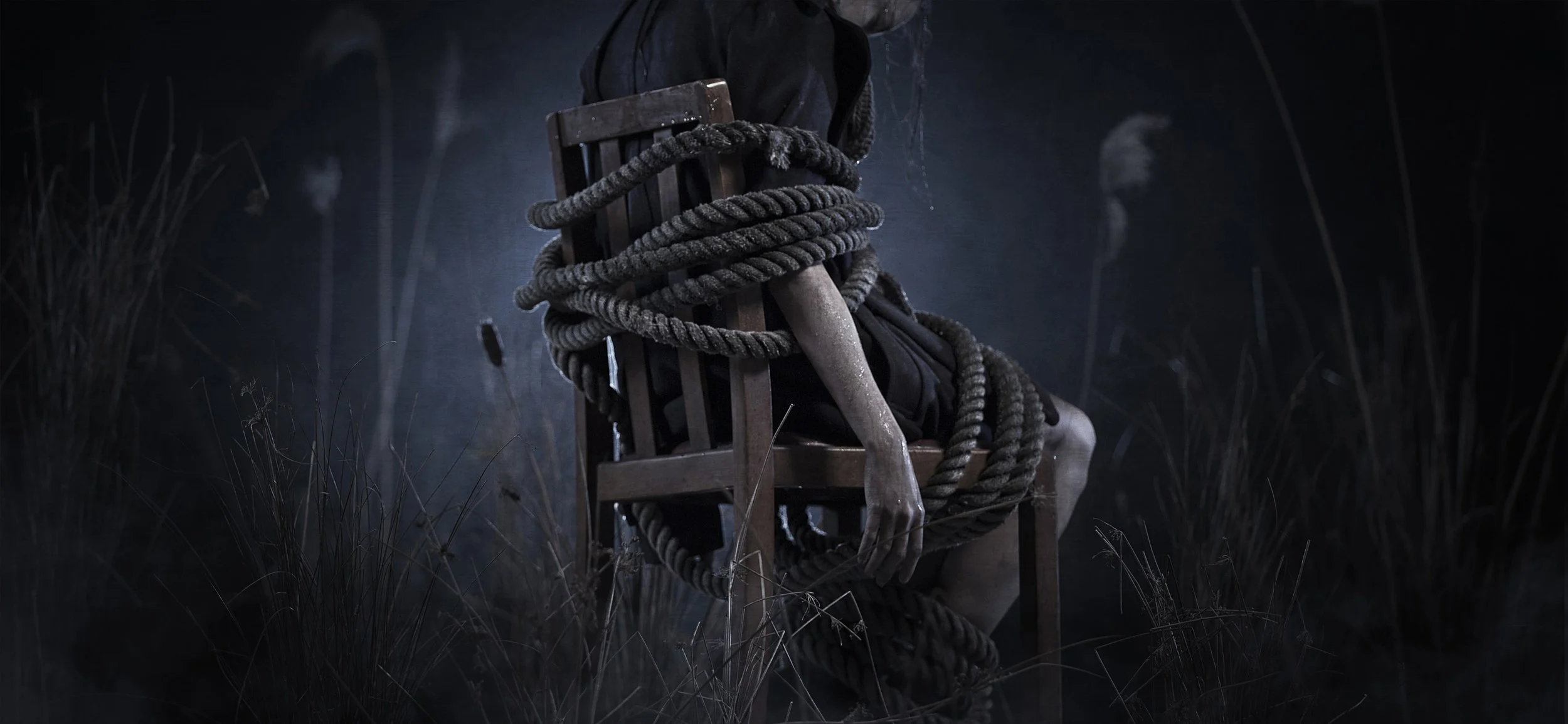 Promotional image for the video game Murdered, based on the salem witch trials. We see a woman tied to a chairwith thick rope, dripping wet and in a dark setting with grass and reeds in the background. commercial photography by Steve Bright, London