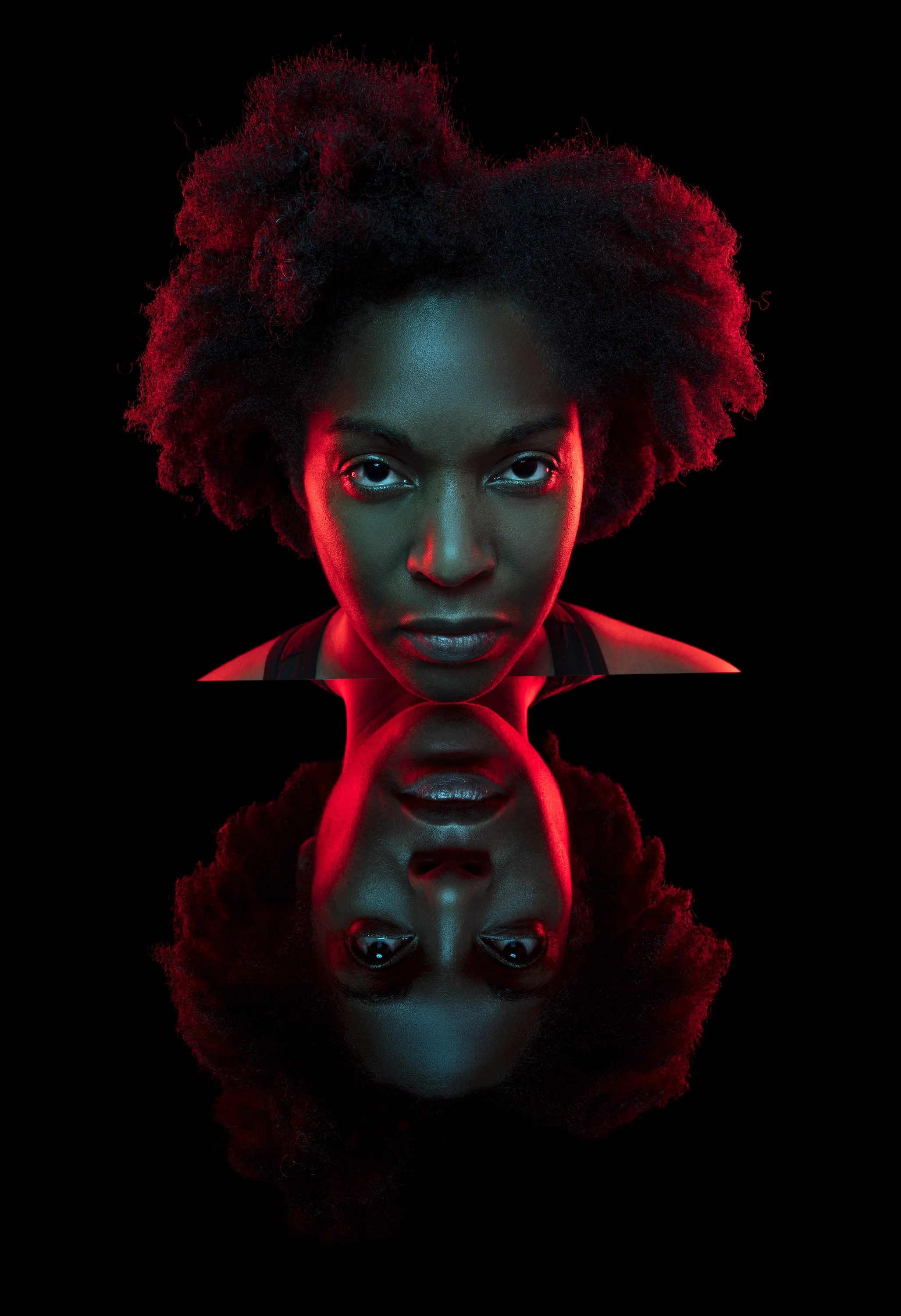 A Black woman with an afrostares into camera, her chin resting on a black mirror so that we see her face and it's reflection. stylised commercial portrait photography by Steve Bright