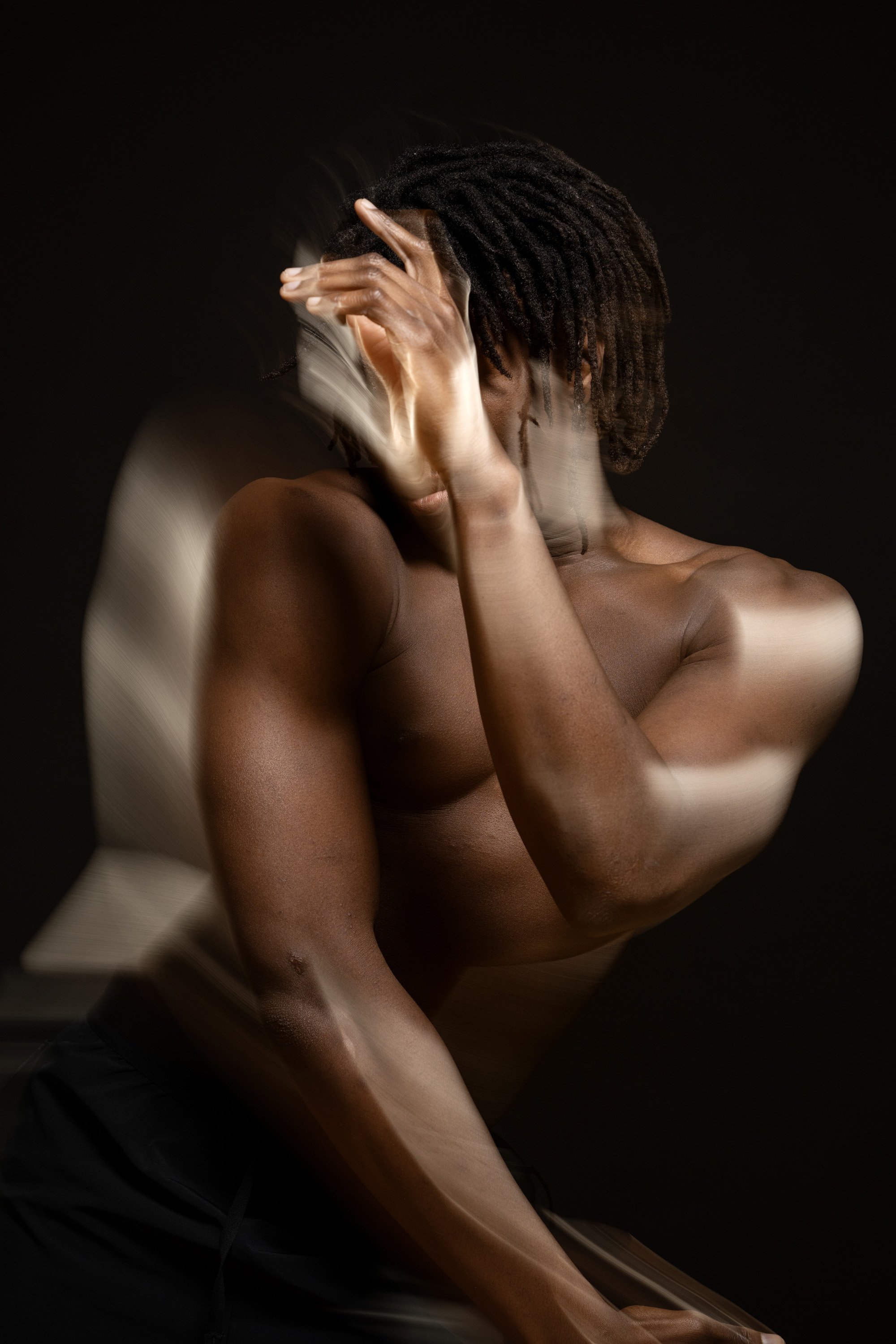 A shirtless man with dreadlocks, with his eyes closed, dancing in a dark space with motion blur around the edges of his body. dynamic sports  portrait photography by Steve Bright.
