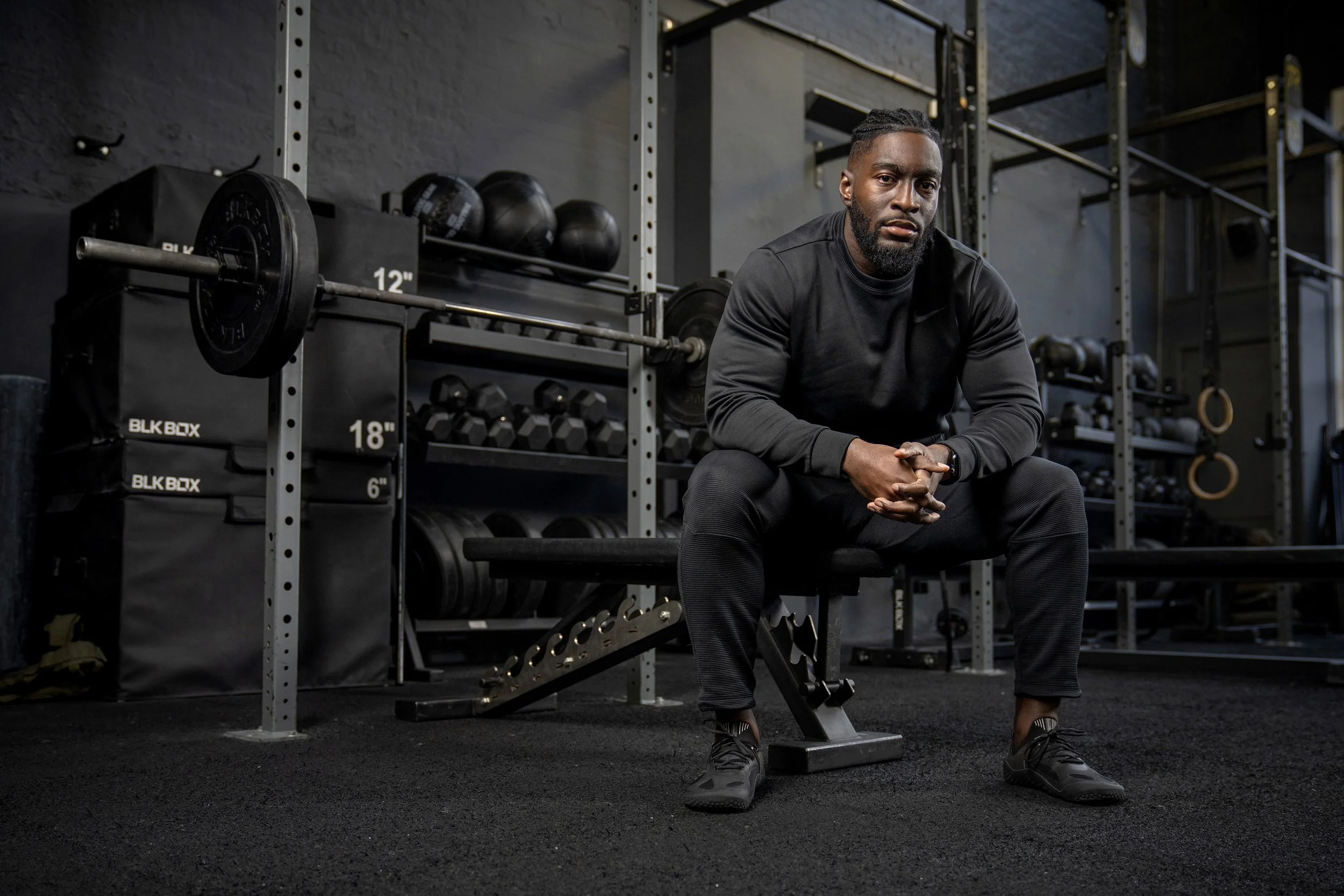 A man sitting on a bench in a gym, surrounded by workout equipment. dynamic sports portrait photography by Steve Bright