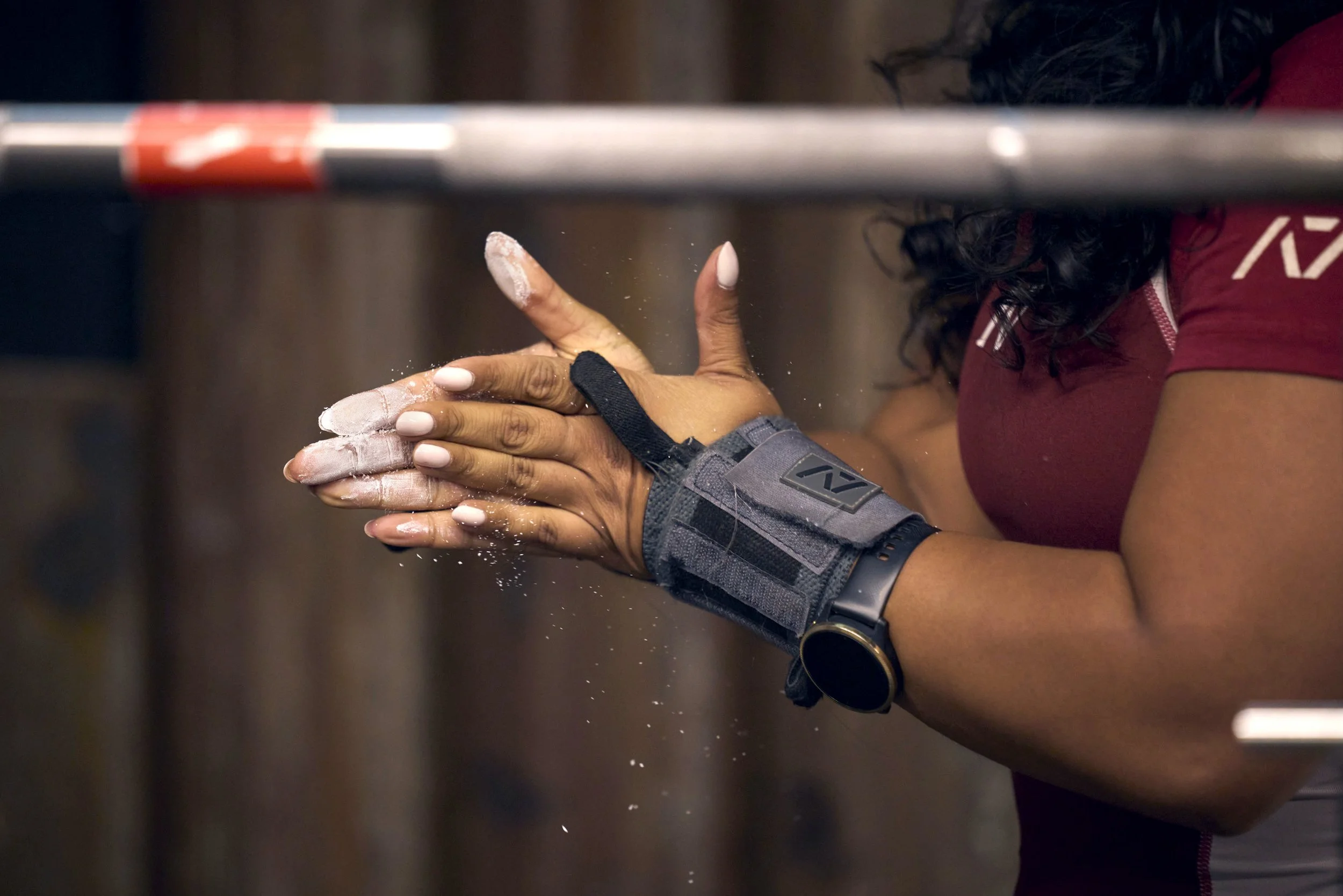 A woman claps her hands together. Her hands are covered in white chalk dust for weightlifting and she is in a gym. A female powerlifter sitting in a gym, surrounded by weightlifting equipment. dynamic sports portrait photography by Steve Bright