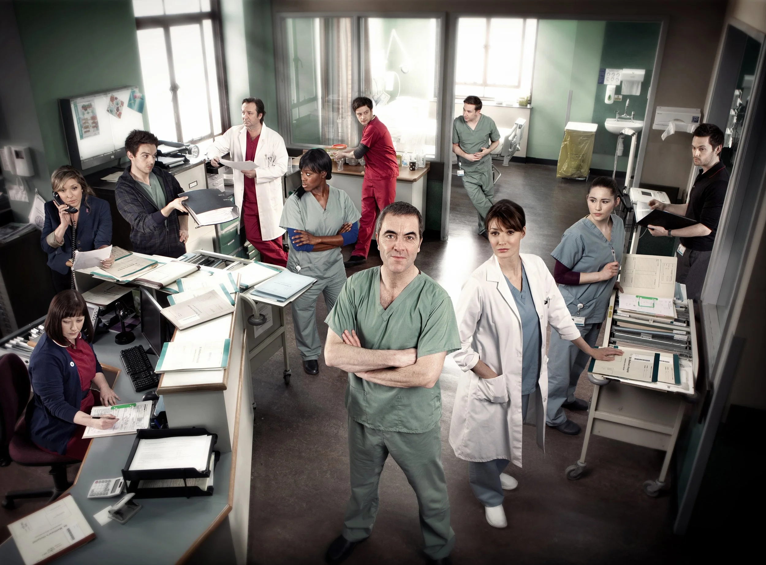 Publicity image for the ITV drama Monroe. The cast are scene in a hospital ward, performing various tasks in the background as James Nesbitt looks into camera. entertainment portrait photography by Steve Bright, London