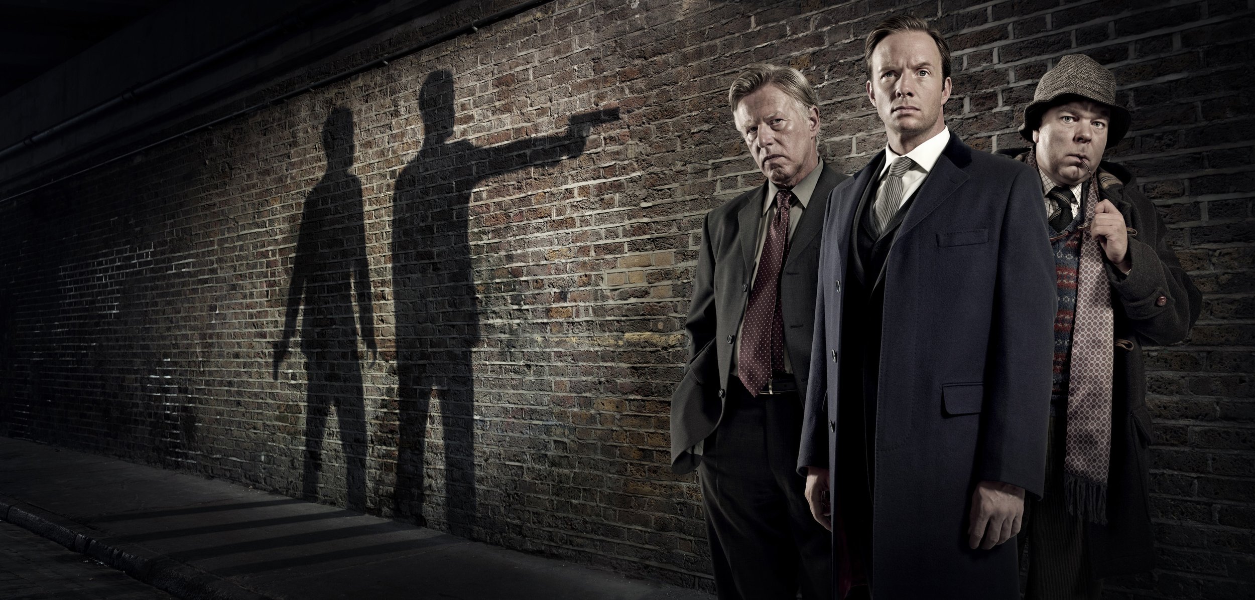 marketing image for the ITV detective drama Whitechapel. The 3 leads stand looking into camera while in the background the shadows of 2 villains point a gun at them. entertainment portrait photography by Steve Bright, London