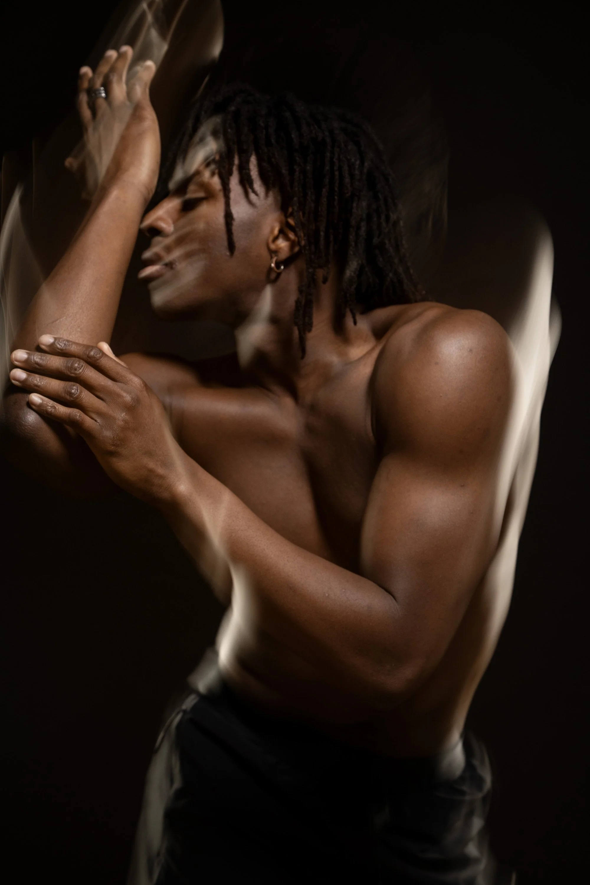 A shirtless man with dreadlocks, with his eyes closed, dancing in a dark space with motion blur around the edges of his body. dynamic sports  portrait photography by Steve Bright.