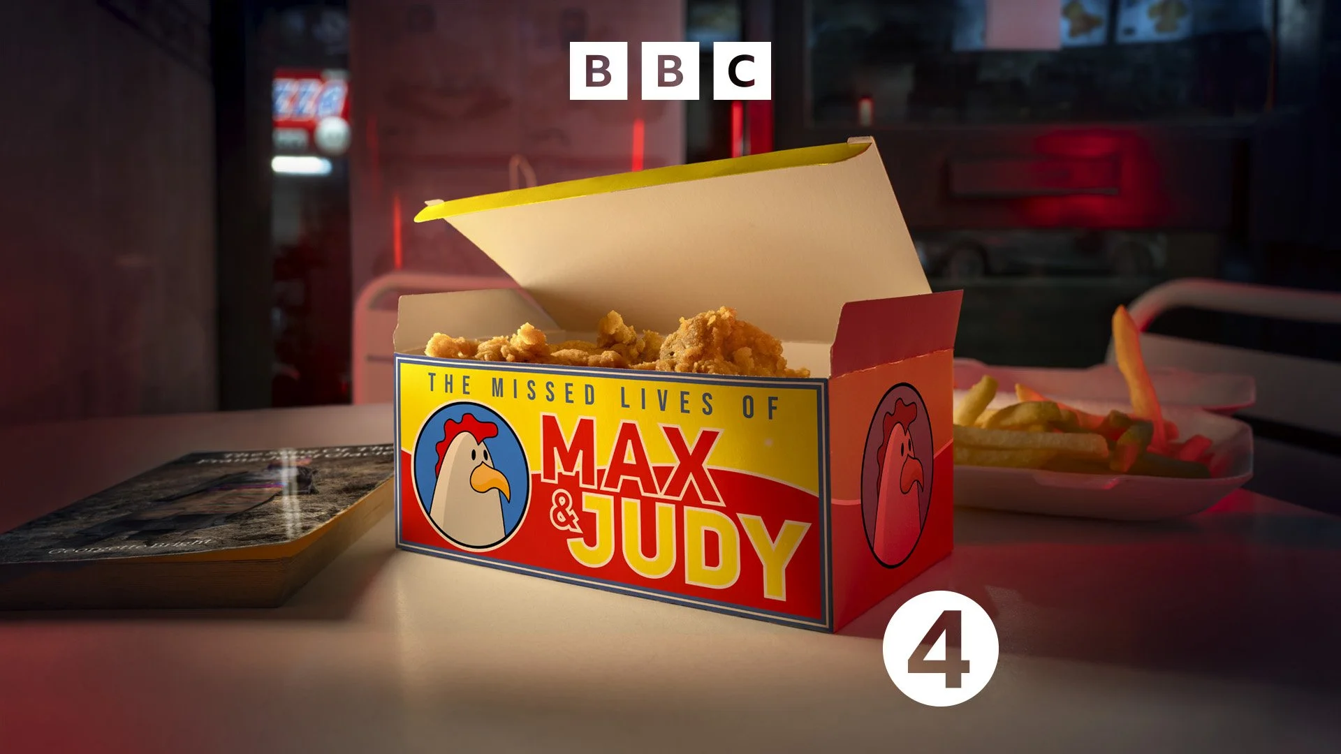 Cover image for the radio play  The Missed Lives of Max and Judy. A box of fried chicken on a table in a high street chicken shop, with the title of the radio play on the side of the box. dynamic entertainment photography by Steve Bright, London
