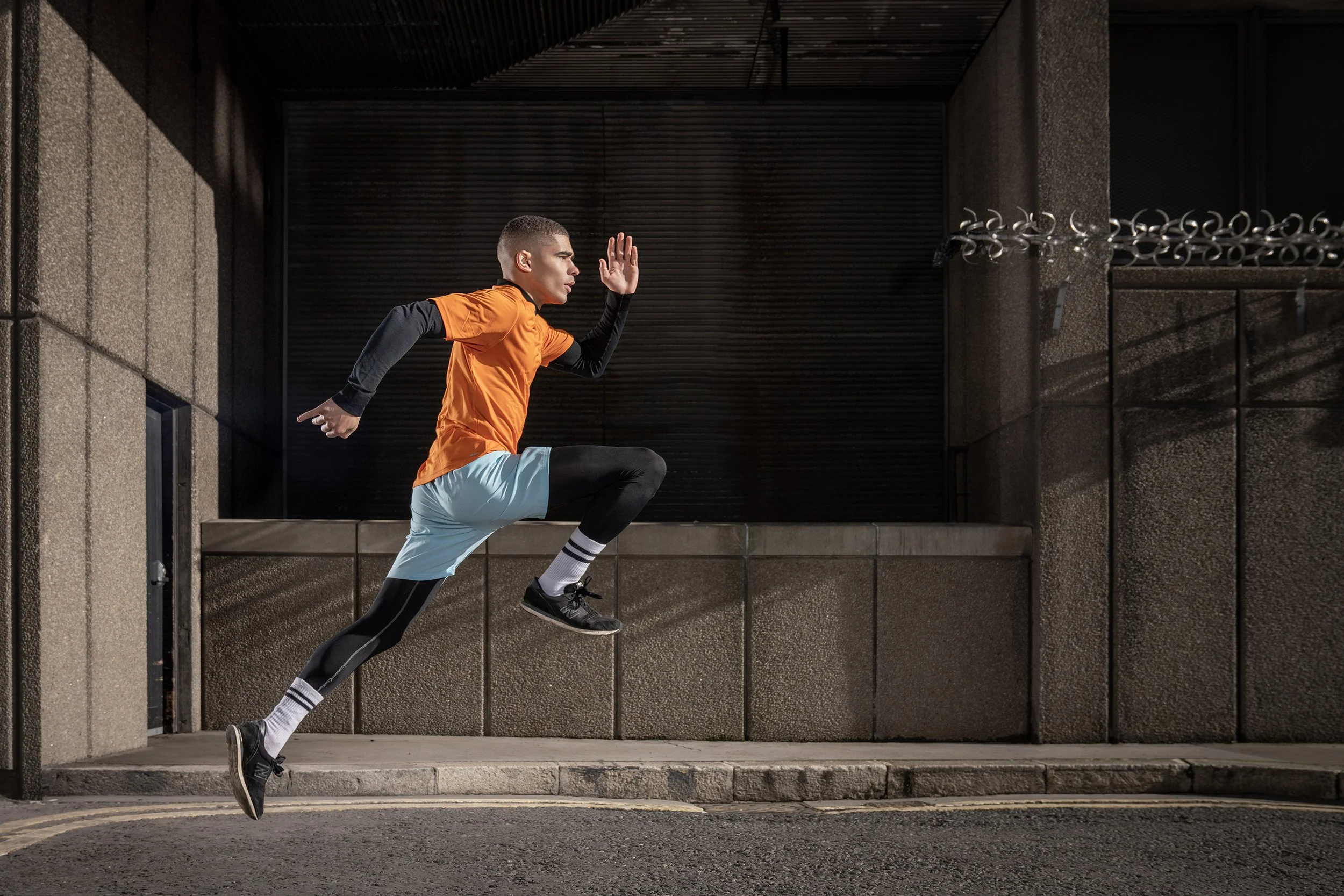 An athlete runs at full speed down an outdoor, urban walkway, wearing a bright orange t shirt.  dynamic sports photography by Steve Bright