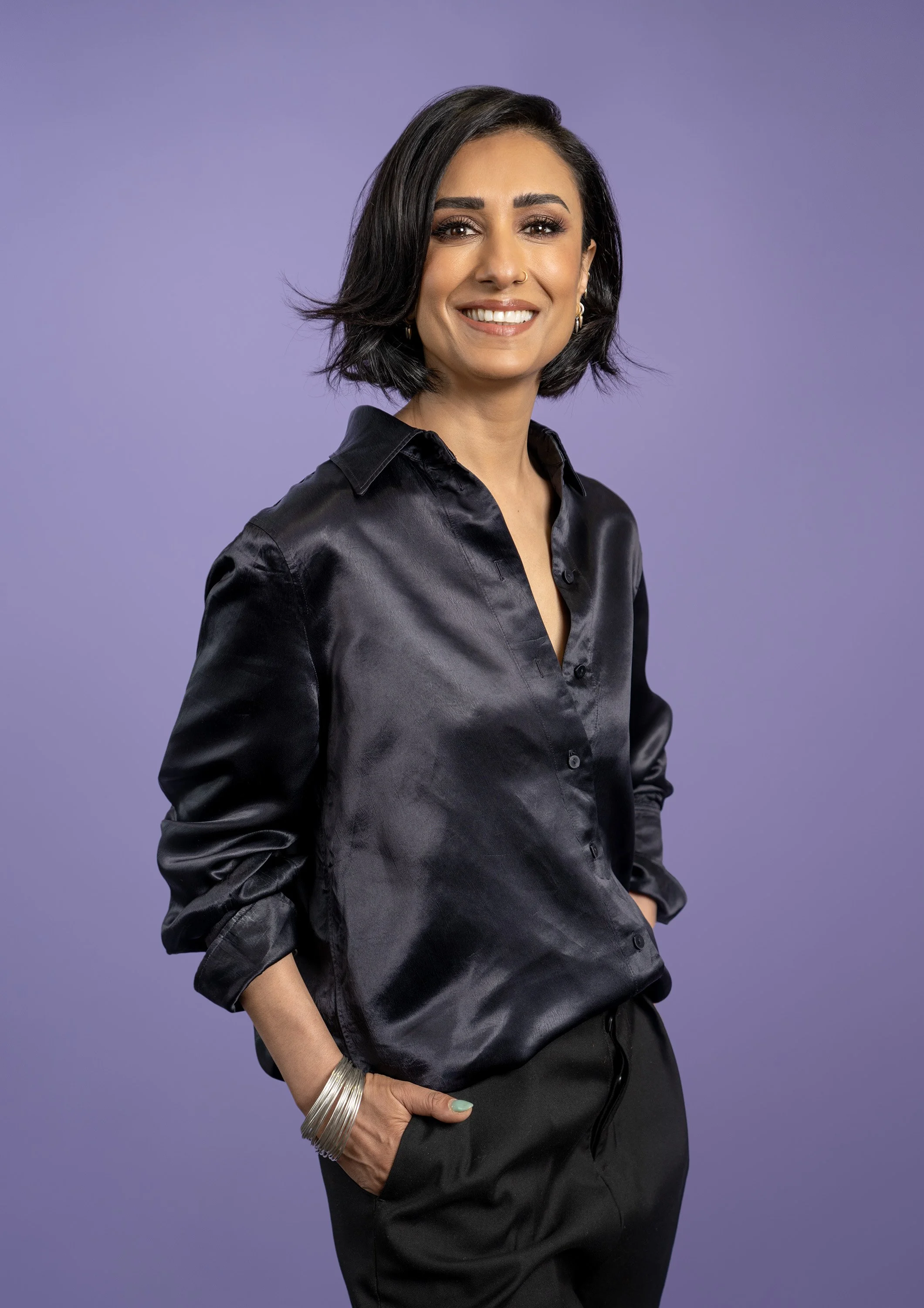 BBC Radio 4's Woman's Hour presenter Anita Rani wearing a black shirt, standing on a purple background. dynamic entertainment portrait photography by Steve Bright London