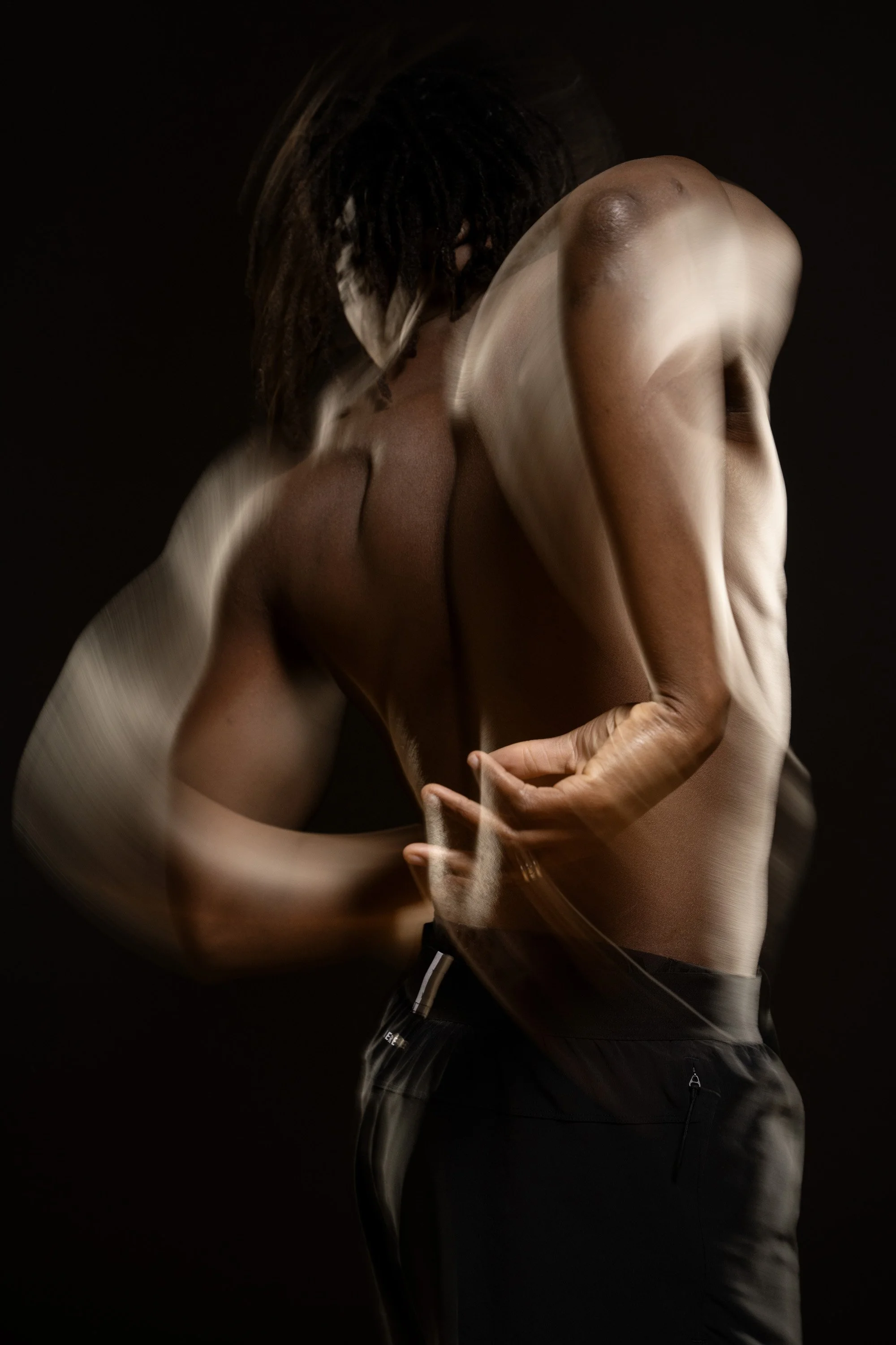 A shirtless man with dreadlocks, with his eyes closed, dancing in a dark space with motion blur around the edges of his body. dynamic sports  portrait photography by Steve Bright.