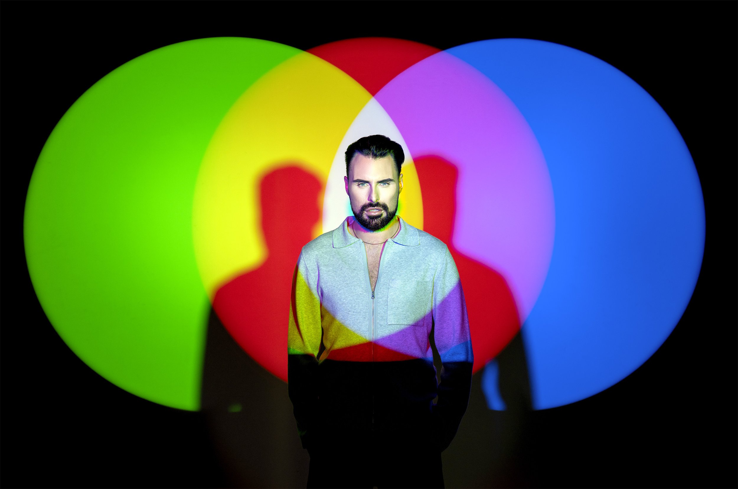 Rylan Clarke stands in the middle of 3 coloured spotlights in a podcast cover image for the BBC podcast How to Be in the Spotlight. dynamic entertainment portrait photography by Steve Bright London