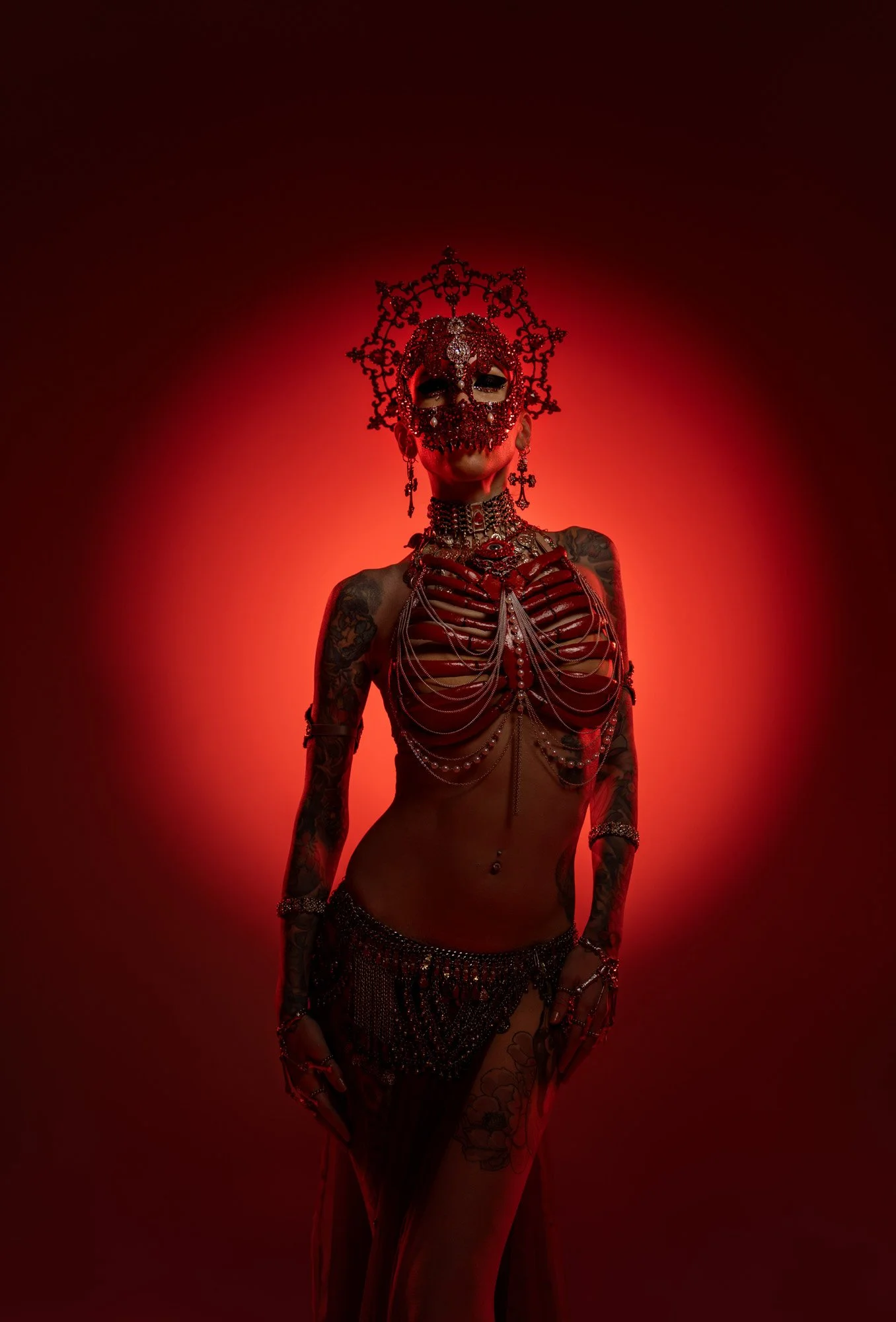 The performer and dancer Leah Debrincat stands, moodily lit, in front of an illuminated red circle background. She wears a jewelled skull headpiece and a chestpiece that looks like a ribcage. entertainment portrait photography by Steve Bright, London