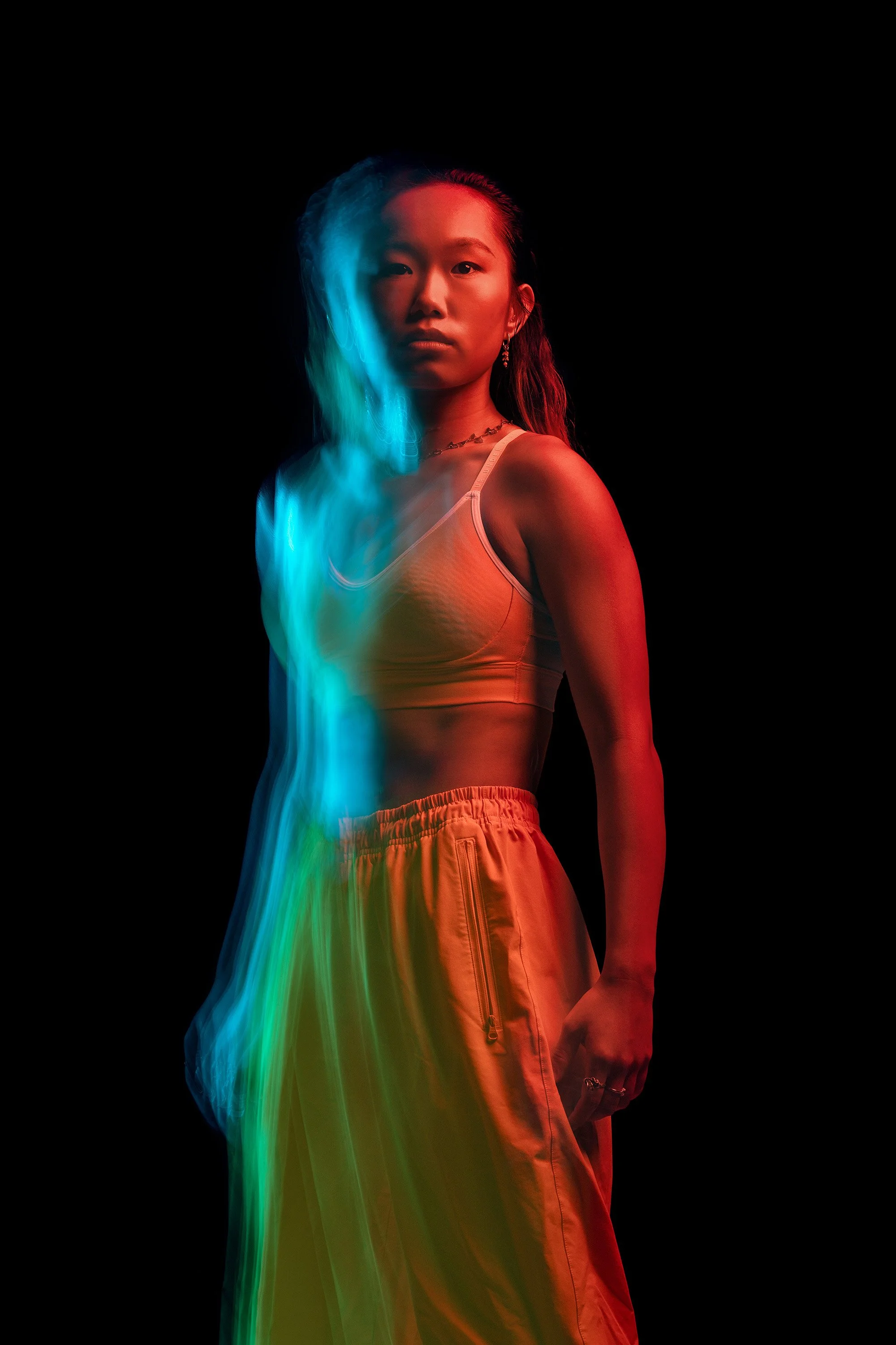 A female martial artist standing against a black background, illuminated with colorful and blurred lights creating a vibrant, artistic portrait. dynamic sports  portrait photography by Steve Bright