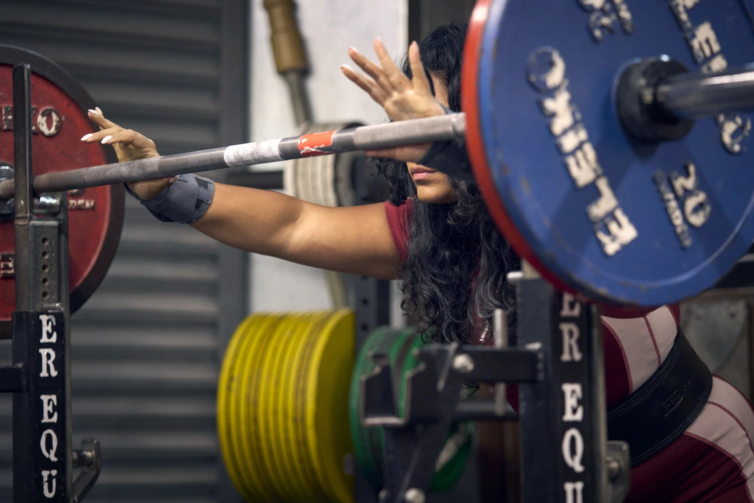 A woman lifting a barbell, surrounded by weight plates and gym equipment. A female powerlifter sitting in a gym, surrounded by weightlifting equipment. dynamic sports portrait photography by Steve Bright