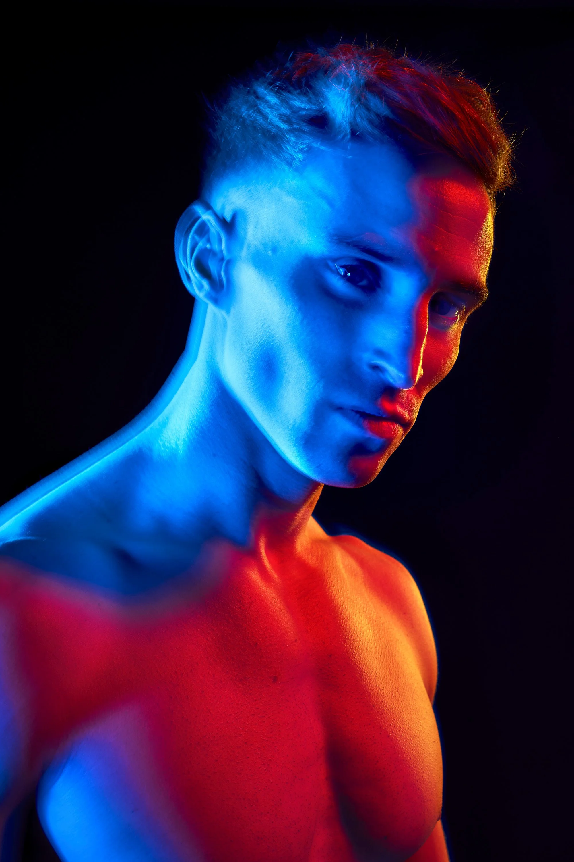 Photo of a topless muscular young man, lit from the left with blurry blue light and from the right with crisp, sharp red and orange light. commercial portrait photography by Steve Bright