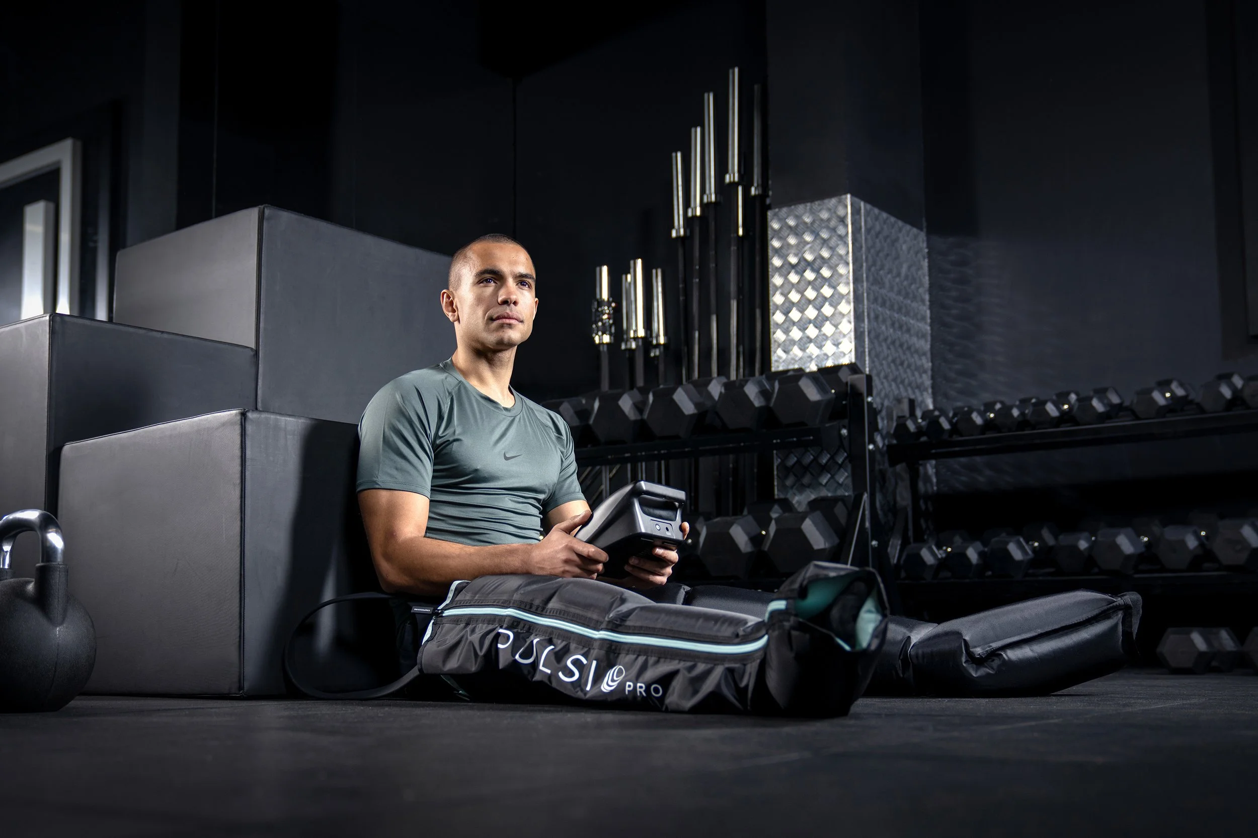 a sporty young man leans against some blocks in a dark coloured gym setting, wearing a pair of pulsio compression boots