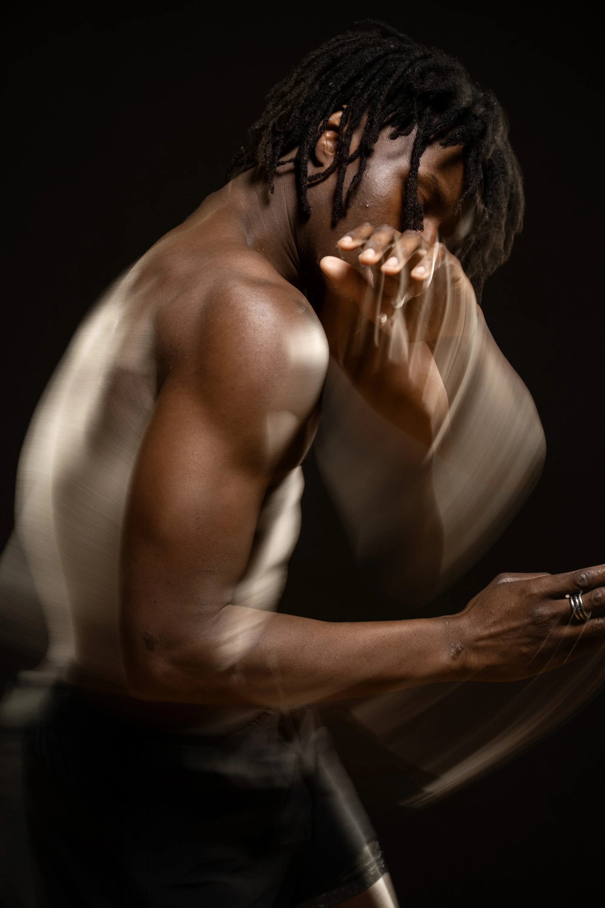 A shirtless man with dreadlocks, with his eyes closed, dancing in a dark space with motion blur around the edges of his body. dynamic sports  portrait photography by Steve Bright.