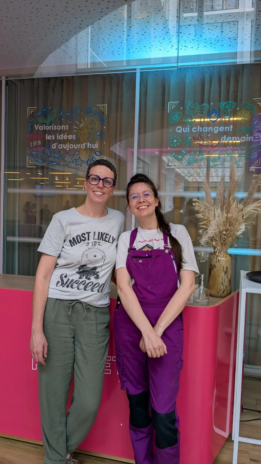 Les illustratrices Sandrine Daniel et Camille Fauquet posent devant deux vitrines peintes à la main réalisées pour les Trophées de l'innovation de l'Apec